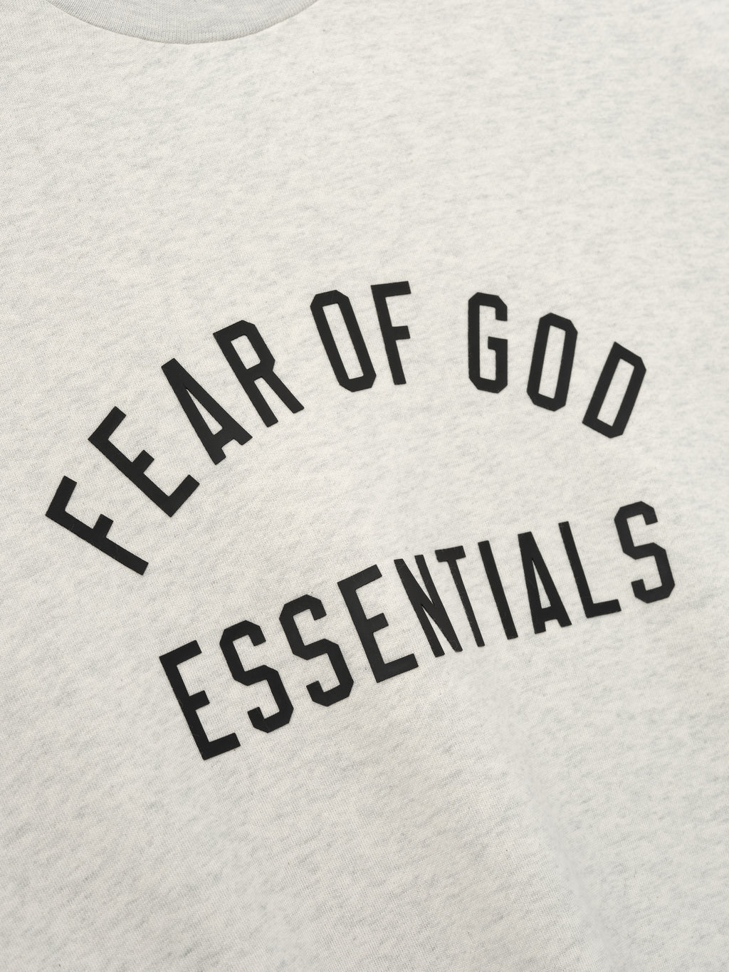 Close-up of light gray fabric with black "FEAR OF GOD ESSENTIALS" text printed in arched style on front panel