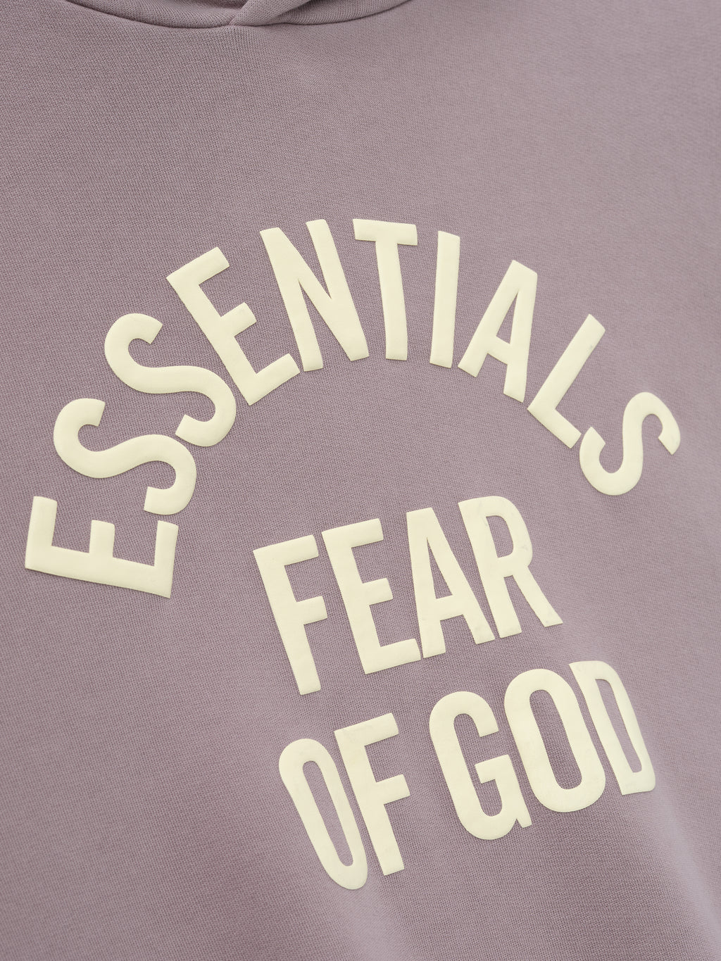 close-up of muted mauve pigment-dyed fleece fabric with raised cream Essentials Fear of God text printed in curved layout
