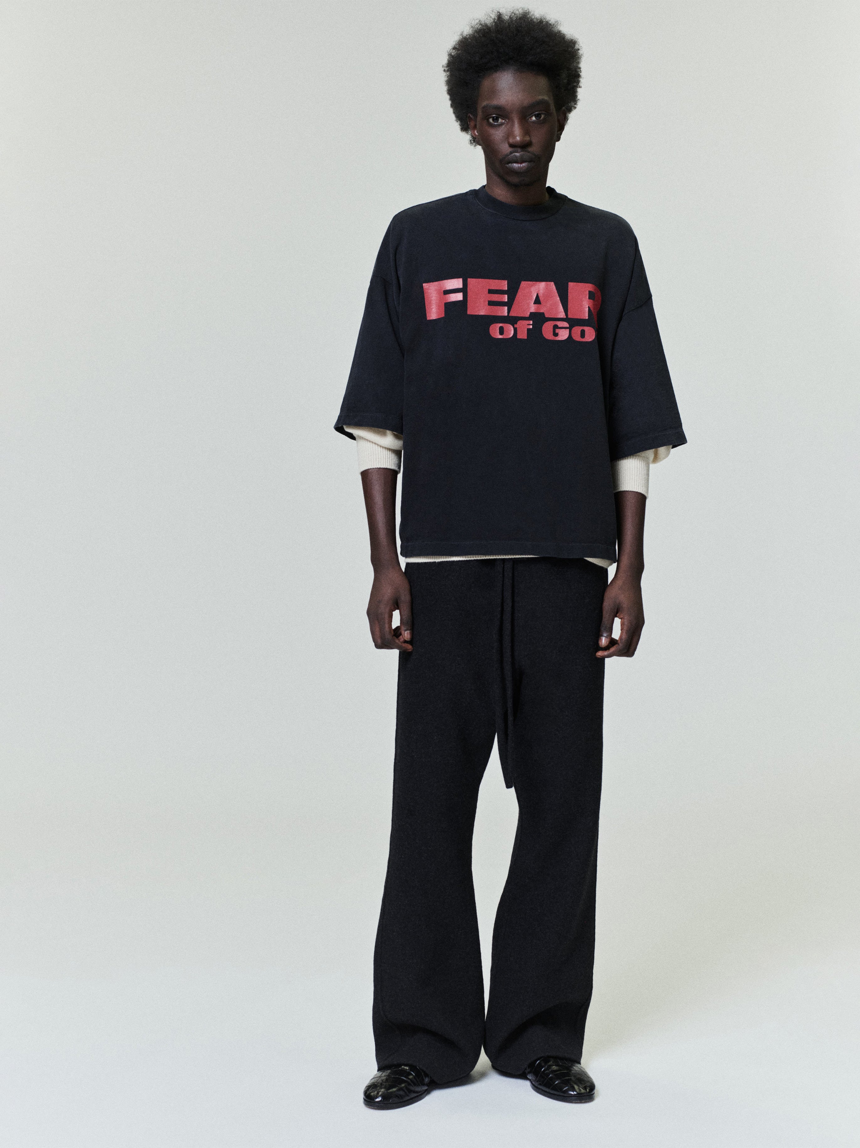 Relaxed Fear Is Gone Tee in black featuring bold red Fear of God lettering, styled with a loose fit and layered over a light long-sleeve top for a contemporary casual look.