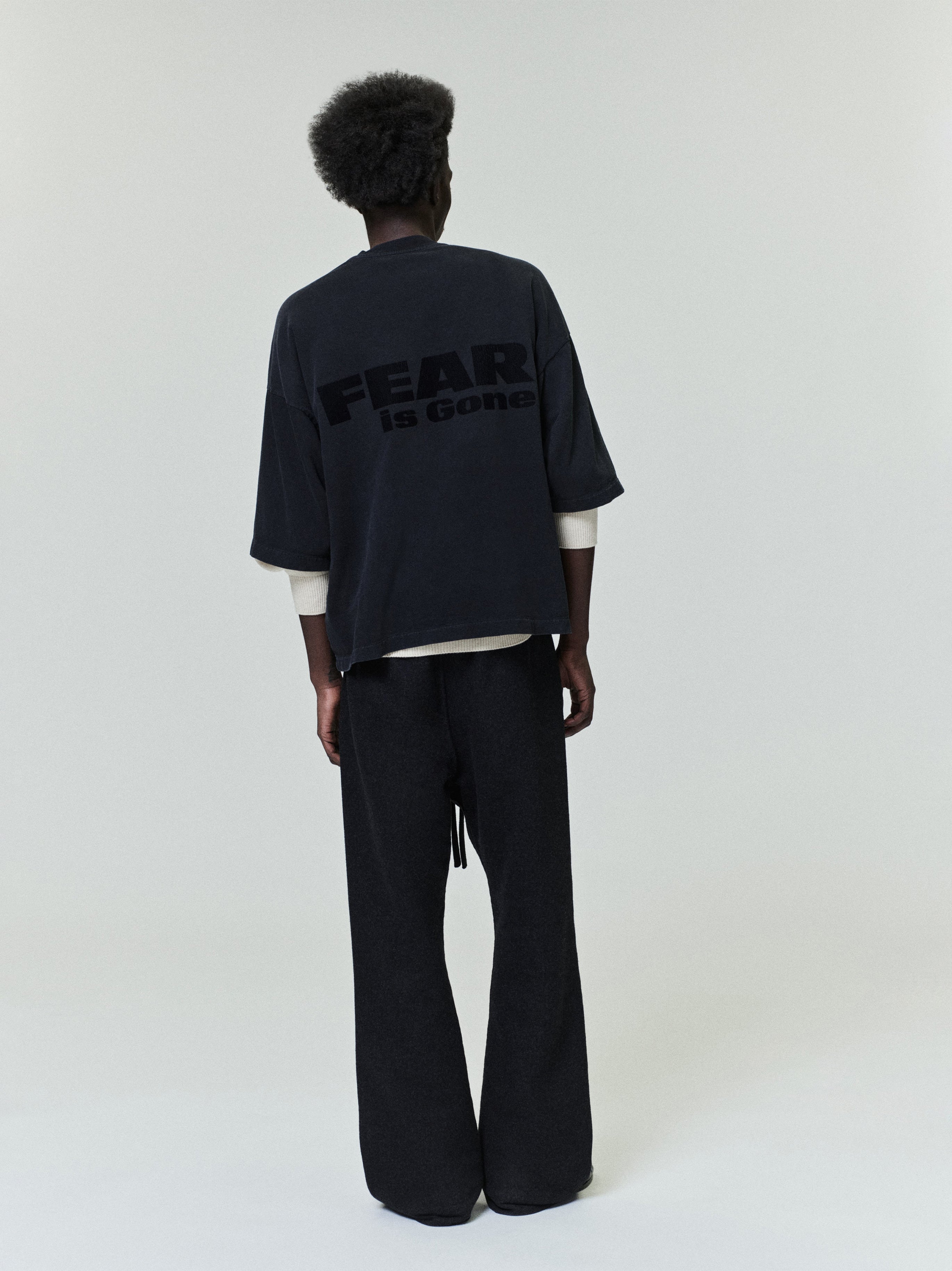 Relaxed Fear Is Gone Tee in dark black featuring oversized lettering on the back, styled with a loose fit layered over a long-sleeve top for a modern casual look.
