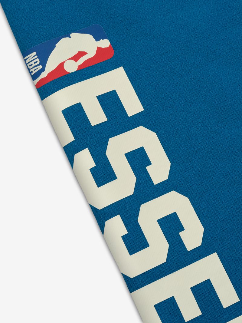 Close-up of blue Knicks Lounge Sweatpant showing white NBA ESSENTIALS text and official NBA logo near waistband edge