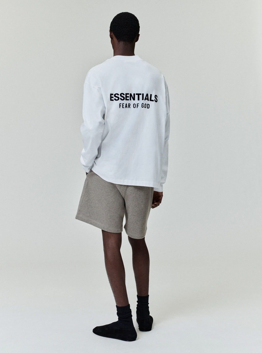 Rear view of model wearing white Classic Long Sleeve Tee with black ESSENTIALS Fear of God logo, image A10_A4_3411.jpg gallery 0