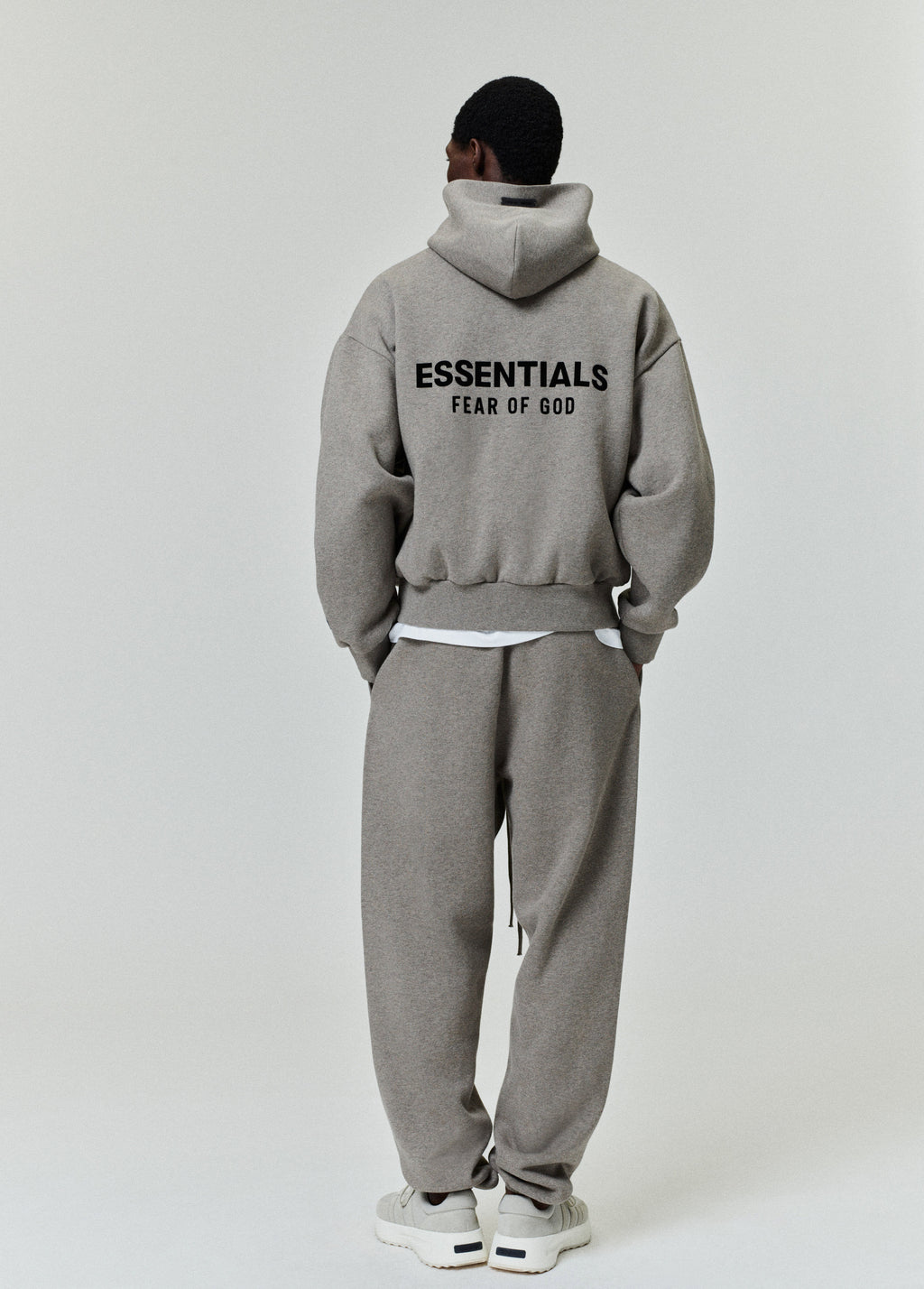 rear view of grey Essentials Classic Hoodie with bold black logo on back paired with matching sweatpants and sneakers