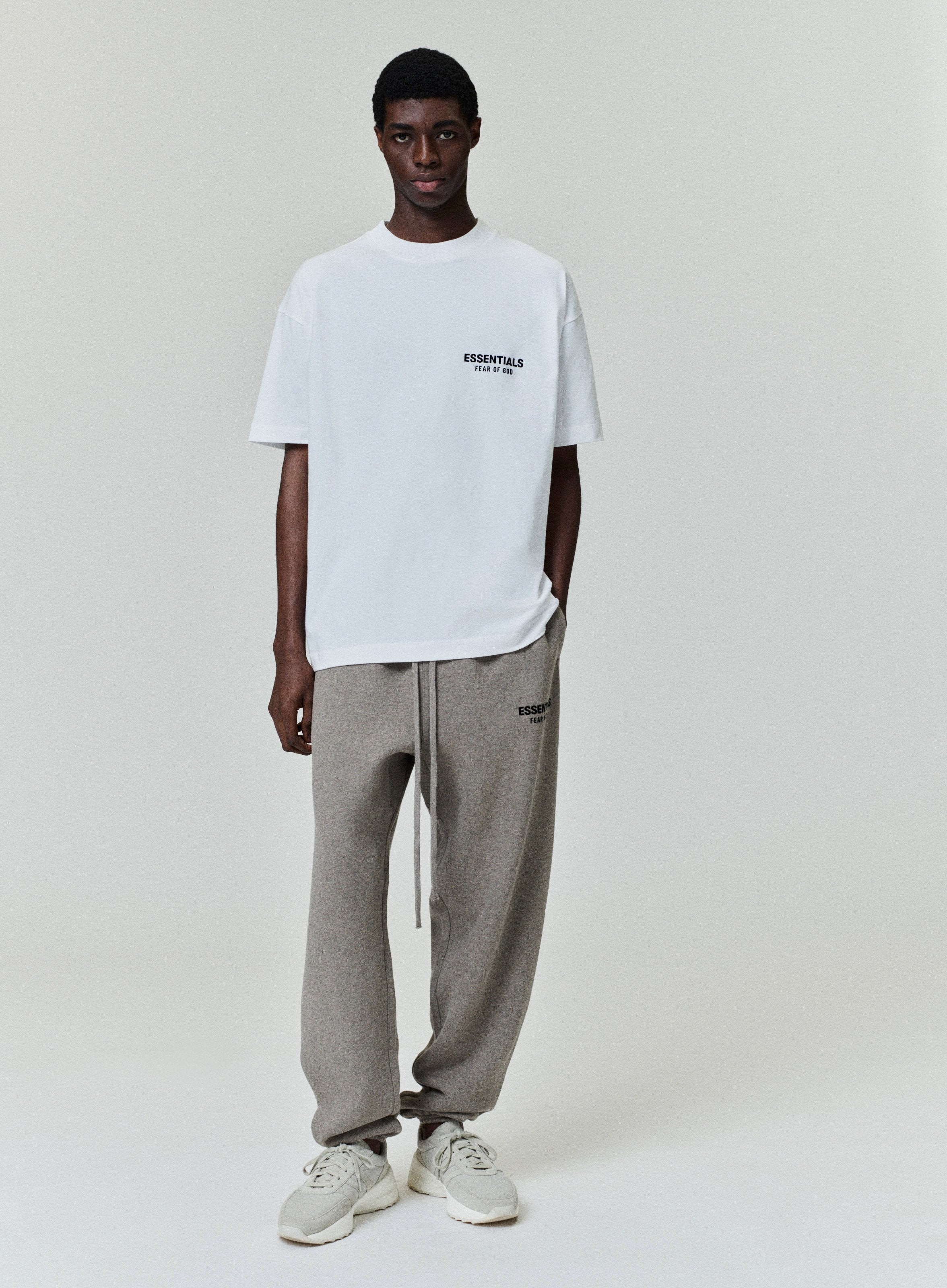 Model wearing a white Essentials Fear of God T-shirt with gray sweatpants against a light background.