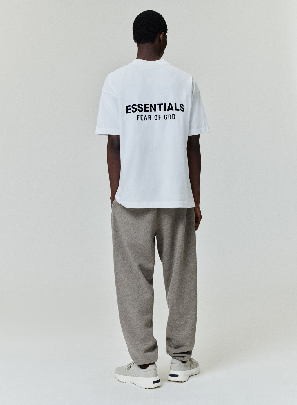 Model wearing a white Essentials Fear of God T-shirt with gray sweatpants against a light background.