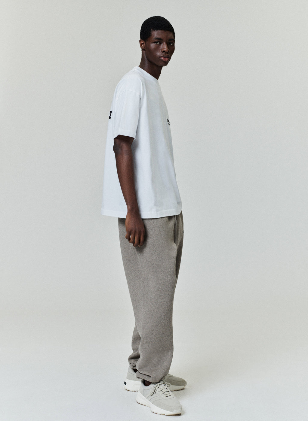 Model wearing a white Essentials Fear of God T-shirt with gray sweatpants against a light background.