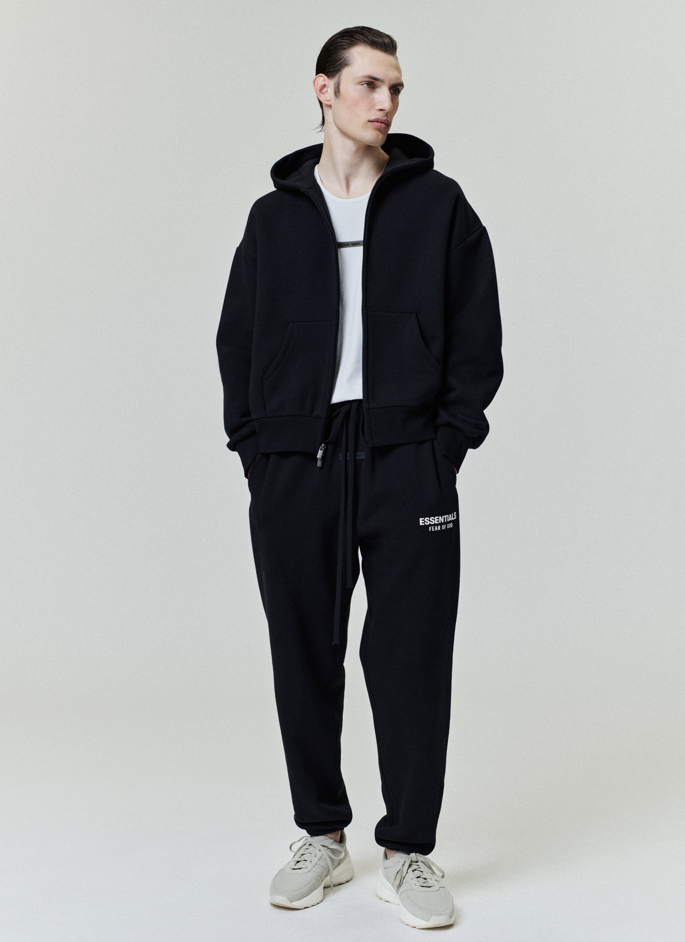 Full frontal view of model in black Classic Full Zip-Up Hoodie with hood up, paired with matching ESSENTIALS sweatpants, gallery image 0