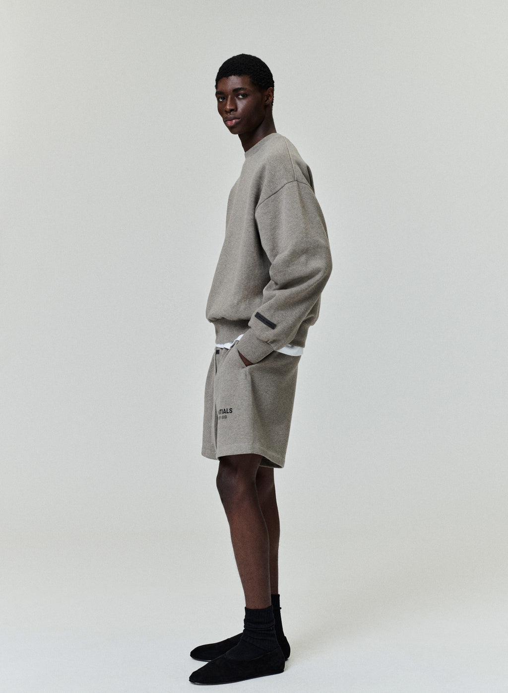 Side profile of model wearing light gray Classic Sweatshort with hand in pocket against plain background