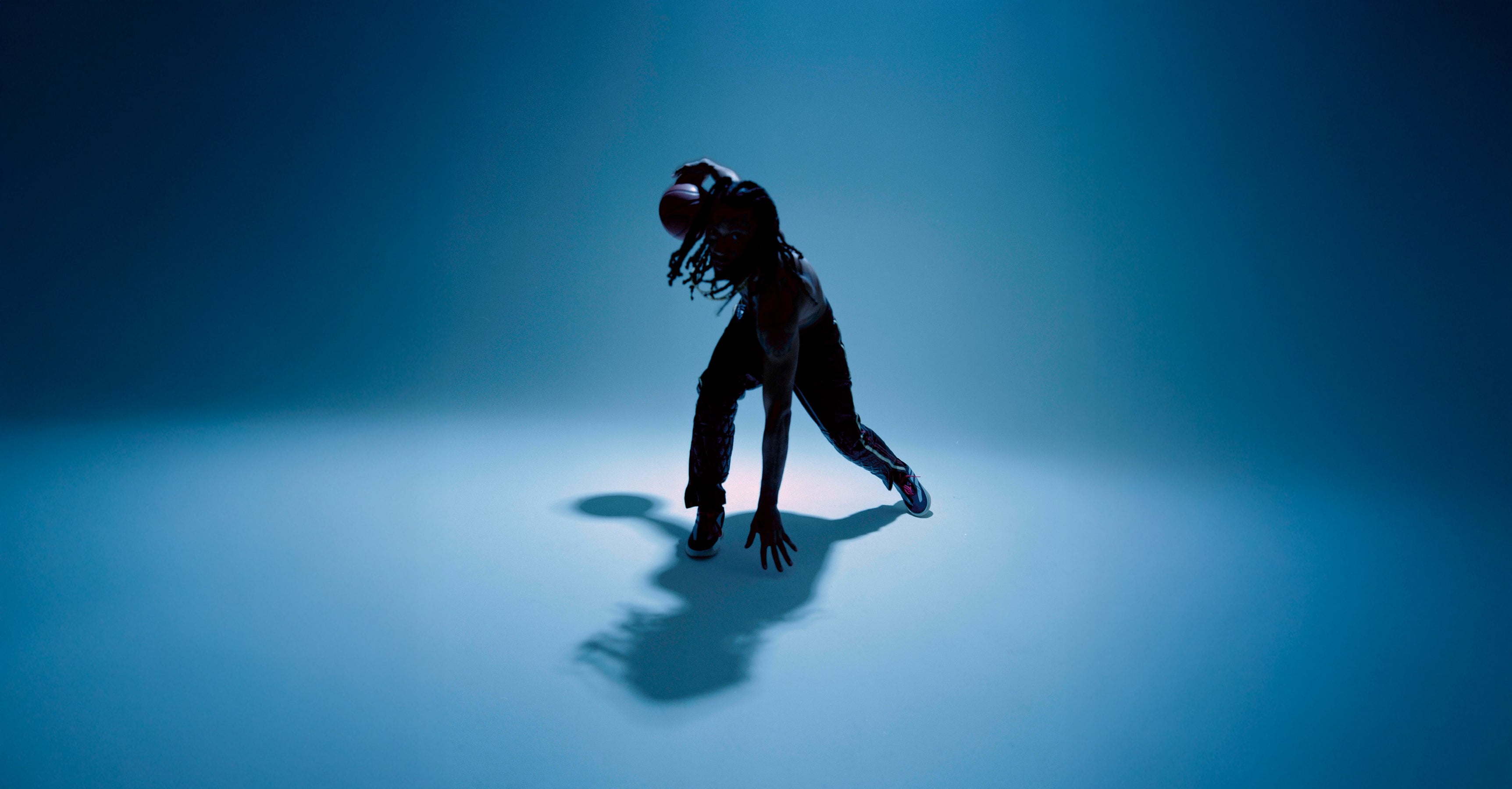 Person wearing virtual reality headset leaning forward with hands on the ground in a dark, blue-lit space