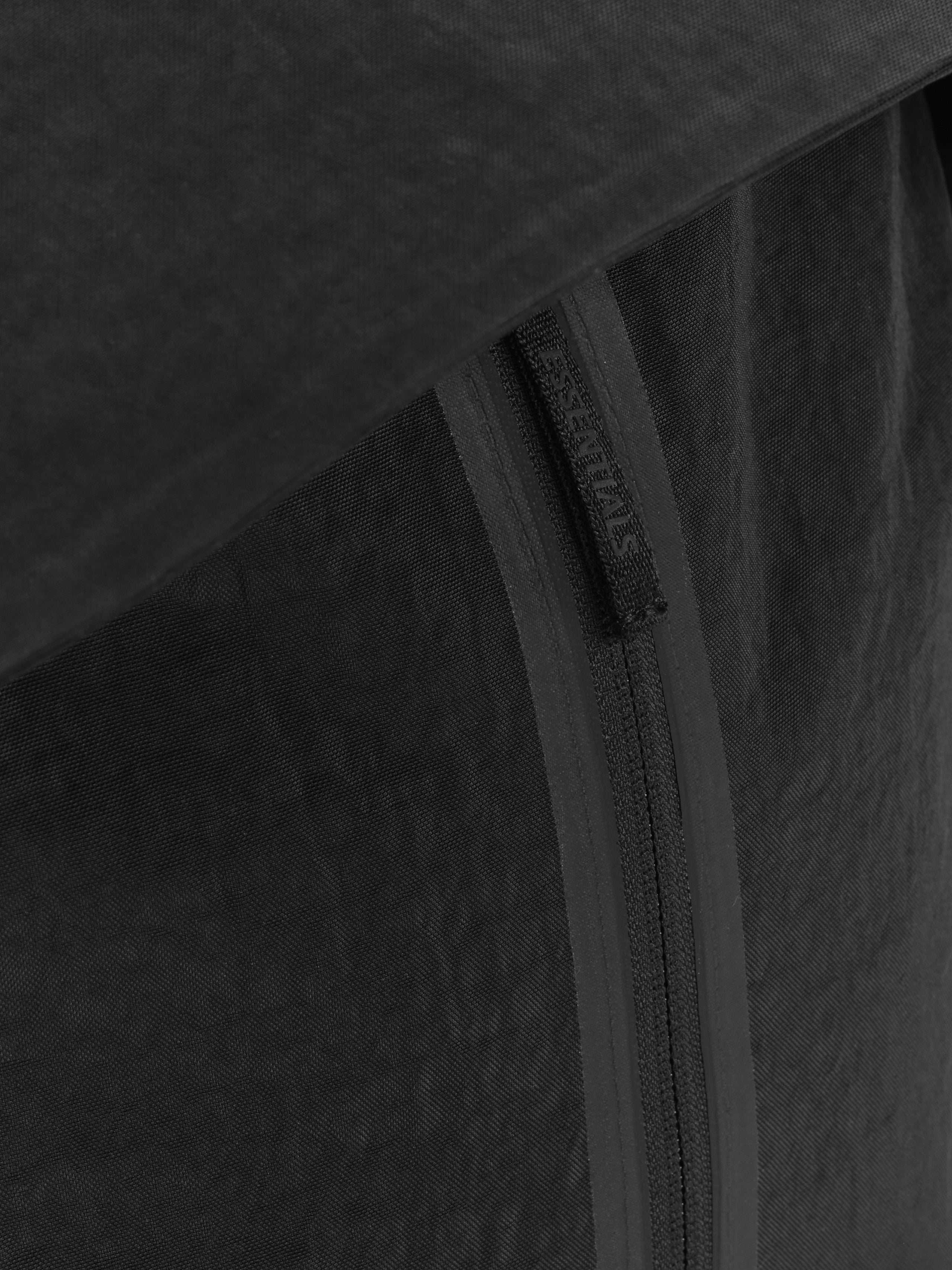Essentials Backpack in black close up highlighting a vertical zip closure and tonal textured fabric with a subtle logo detail