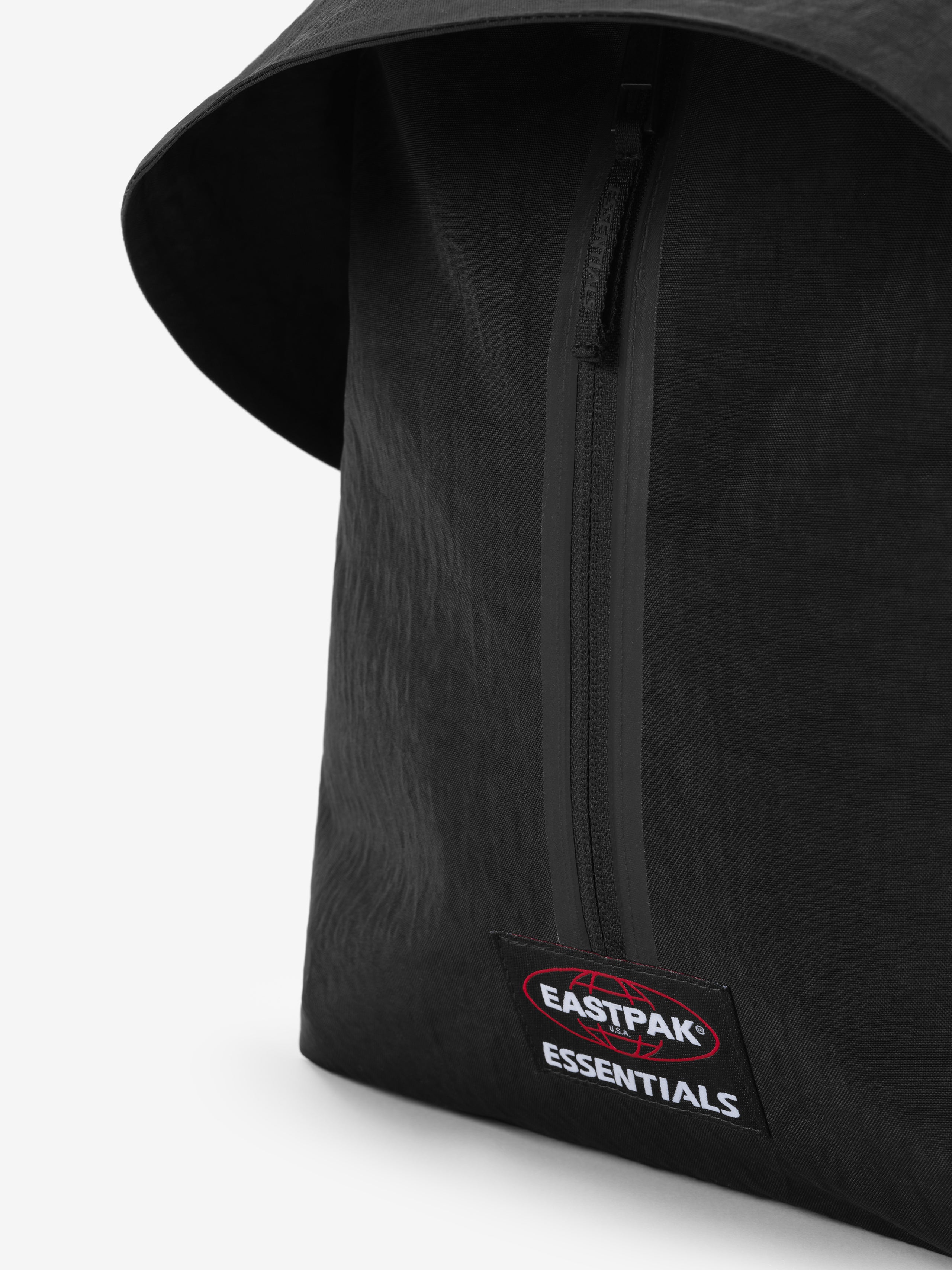 Essentials Backpack in black close up showing a vertical zipper curved top edge and embroidered Essentials logo patch on textured fabric against a white background