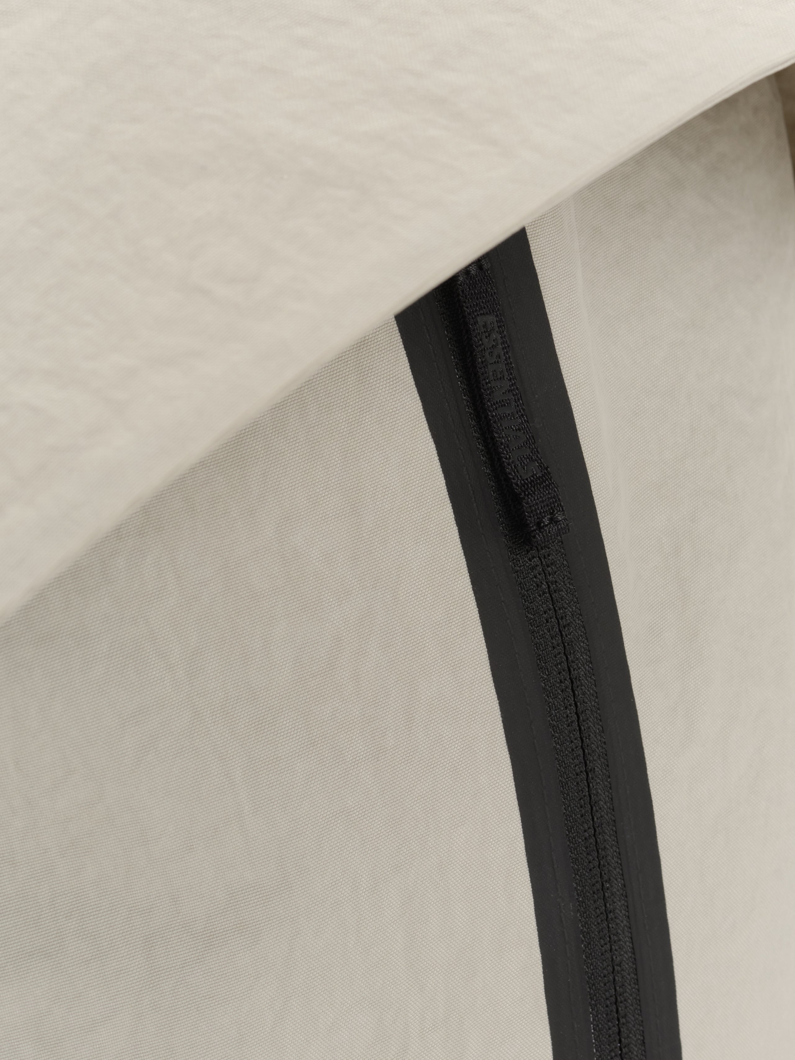 Essentials Backpack close up showing a black zipper set into textured beige fabric with a clean minimalist finish and subtle tonal contrast