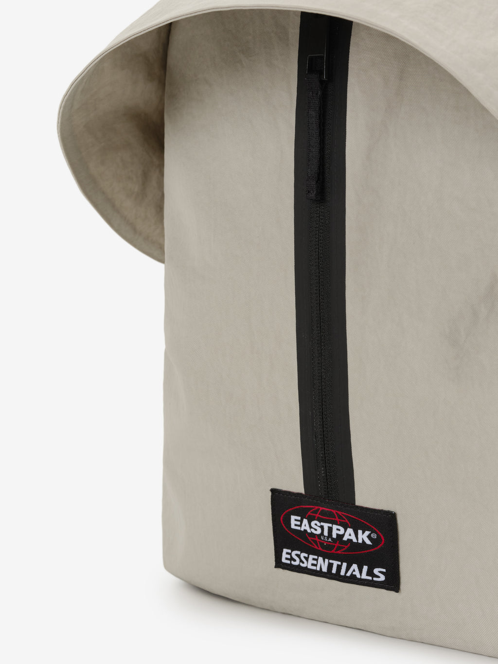 Essentials Backpack in beige close up showing a black vertical zipper and Eastpak Essentials logo patch on smooth fabric with a curved top edge