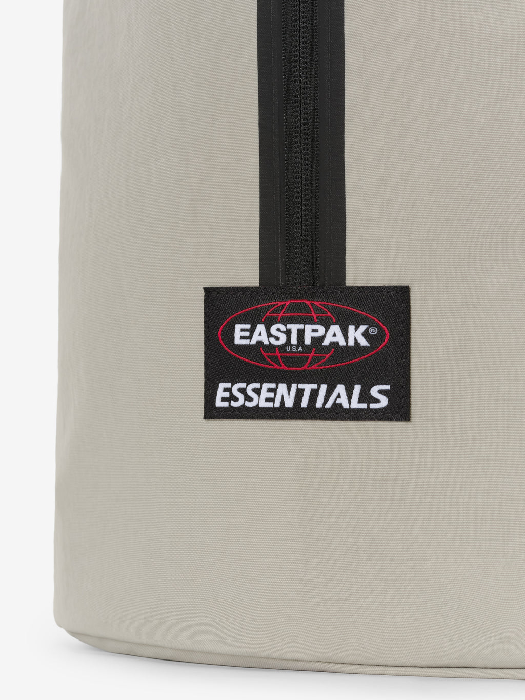 Sports Duffel in light gray close up showing a black vertical zipper and Eastpak Essentials logo patch on smooth textured fabric against a white background