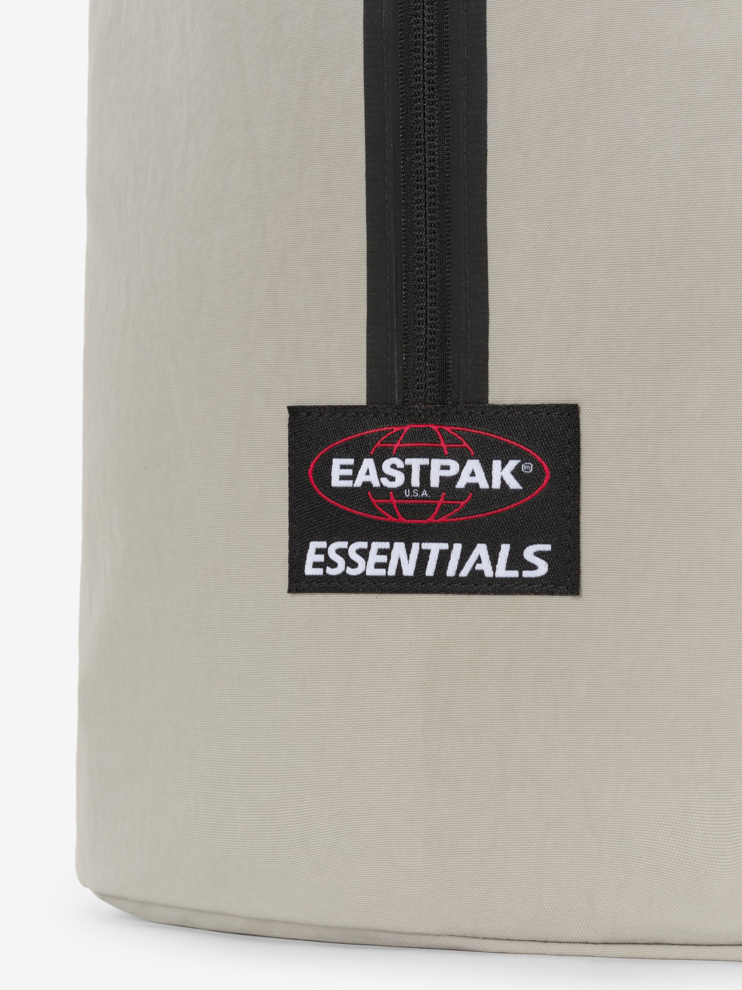 Sports Duffel in light gray close up showing a black vertical zipper and Eastpak Essentials logo patch on smooth textured fabric against a white background