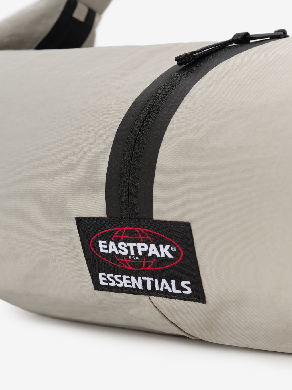 Essentials Shell Bag close up in light beige with a black curved zipper and Eastpak Essentials woven label against a clean white background