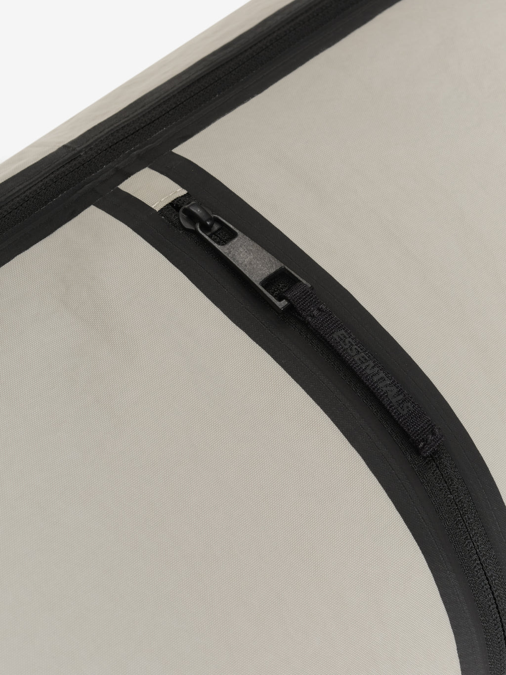 Essentials Shell Bag close up showing a black curved zipper with a metal pull and textured light beige fabric panel