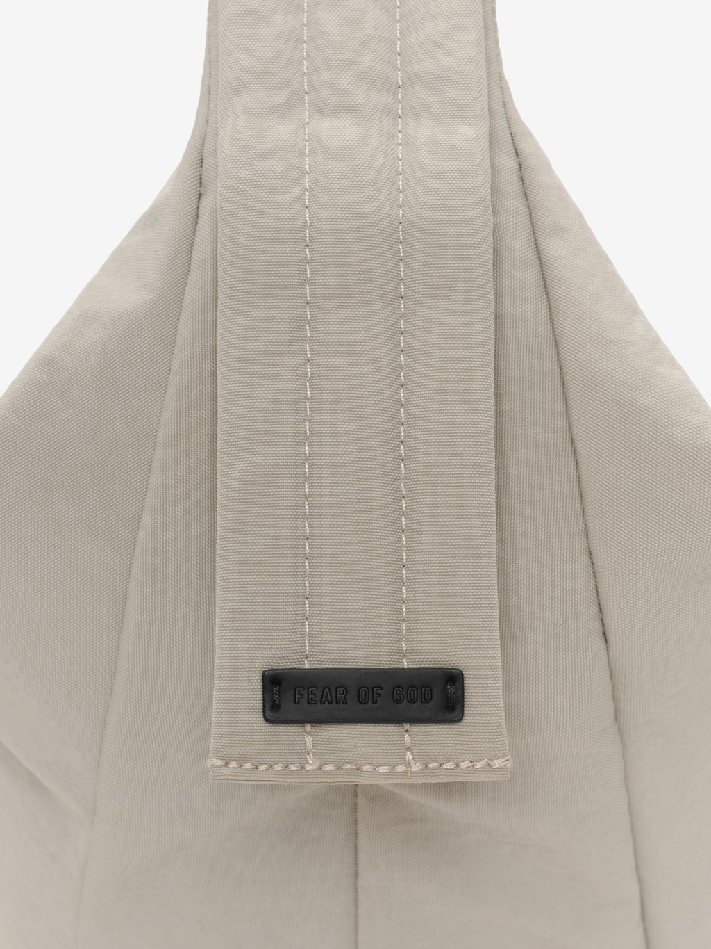 Essentials Shell Bag close up showing a light beige fabric strap with vertical stitching and a black Fear of God label against a plain background