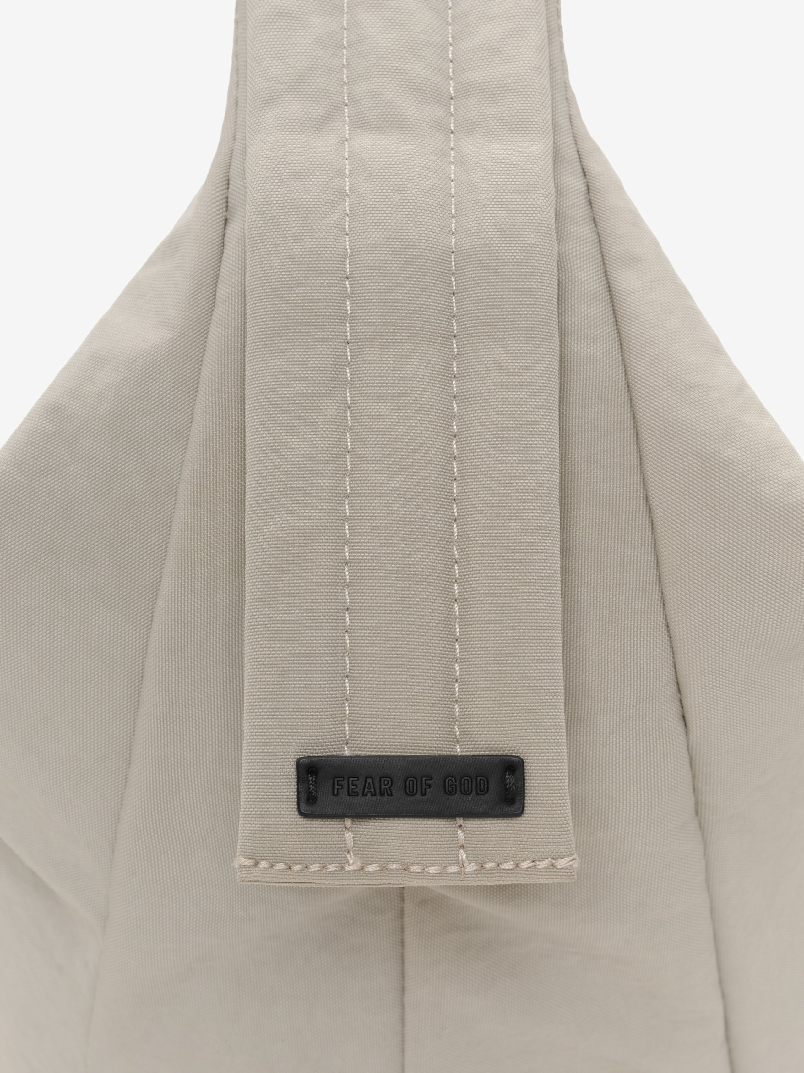 Essentials Shell Bag close up showing a light beige fabric strap with vertical stitching and a black Fear of God label against a plain background
