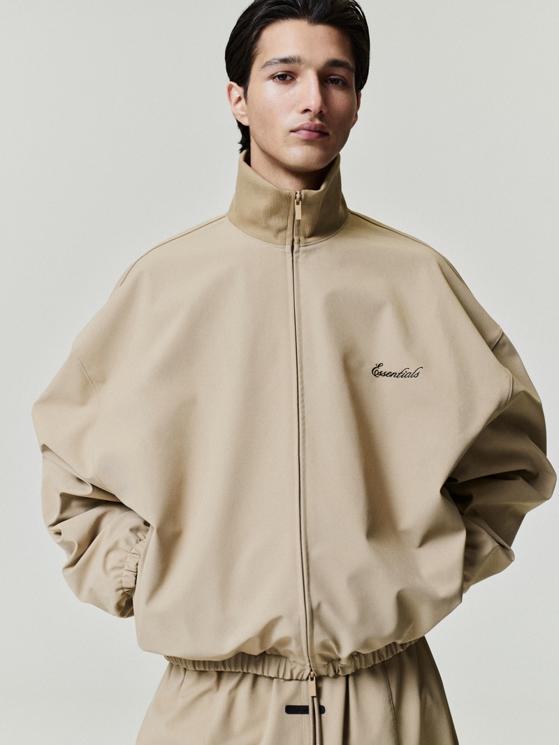 Man wearing a tan tracksuit with a brand logo on a plain background