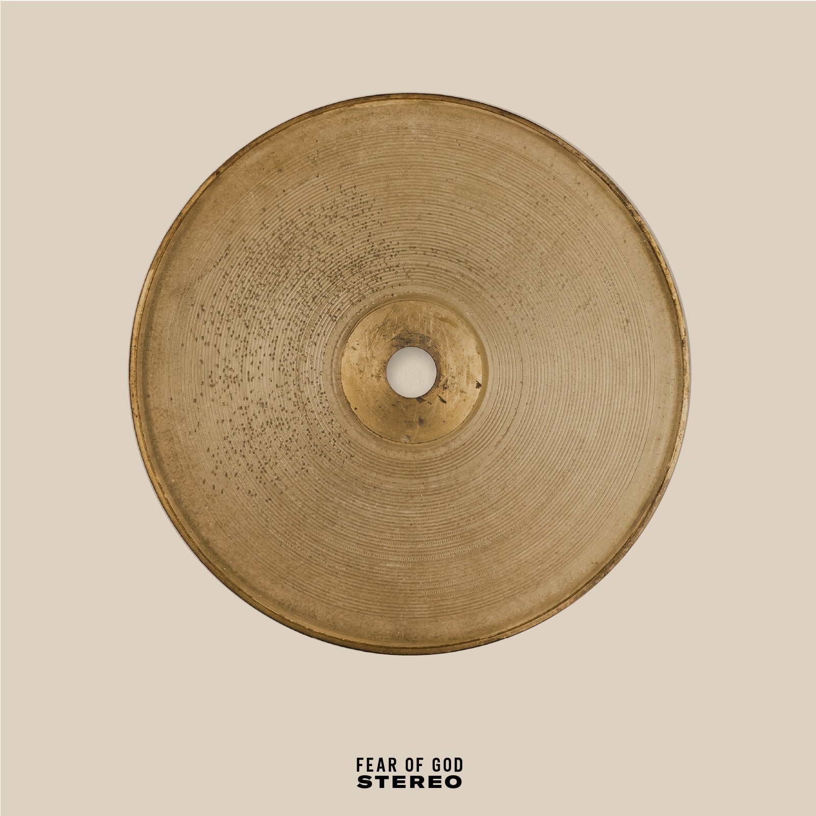 Top-down view of a round, weathered brass cymbal with a hole in the center on a beige background