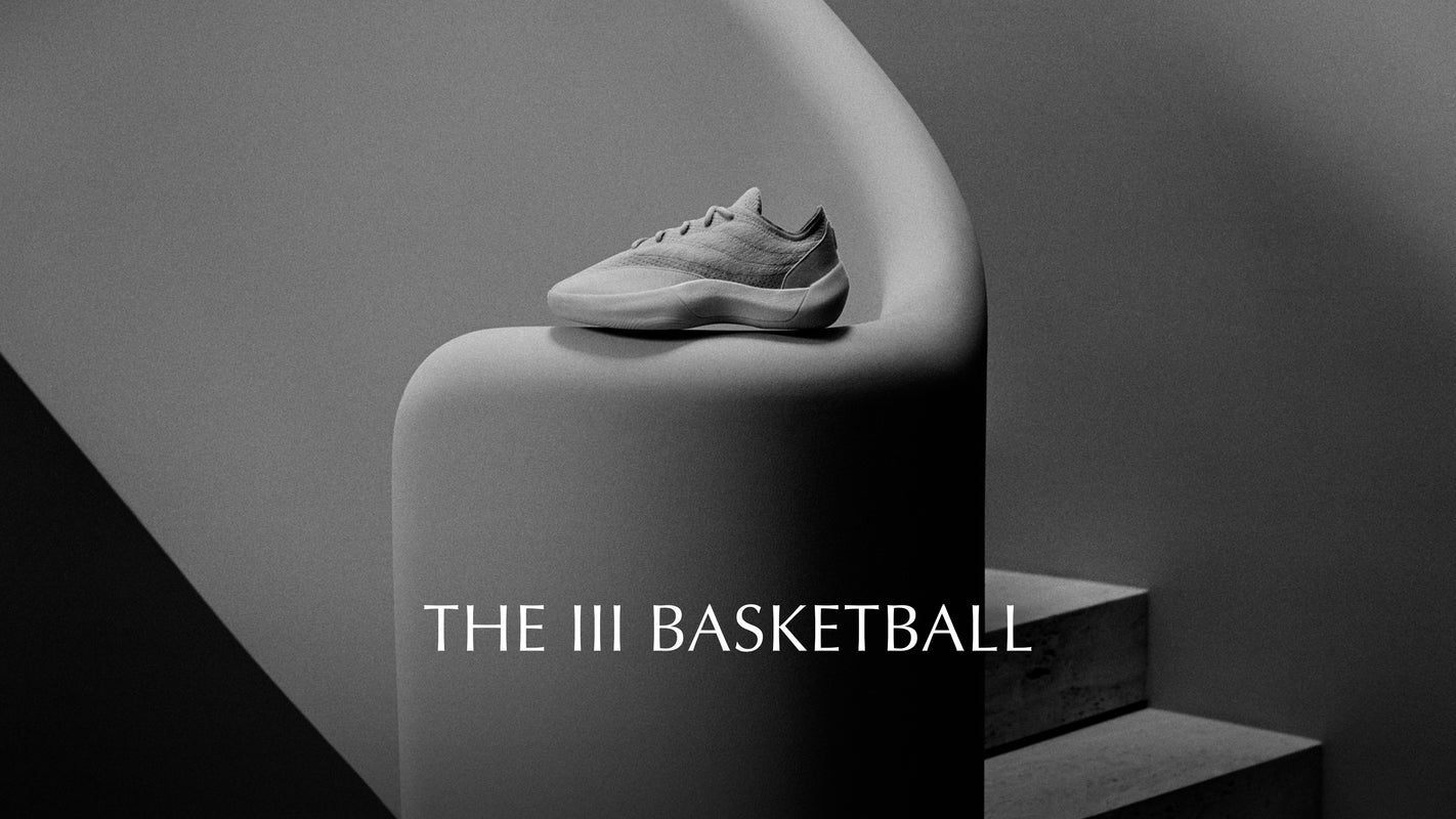 Gray sneaker on a cylindrical white platform with 'THE III BASKETBALL' text.