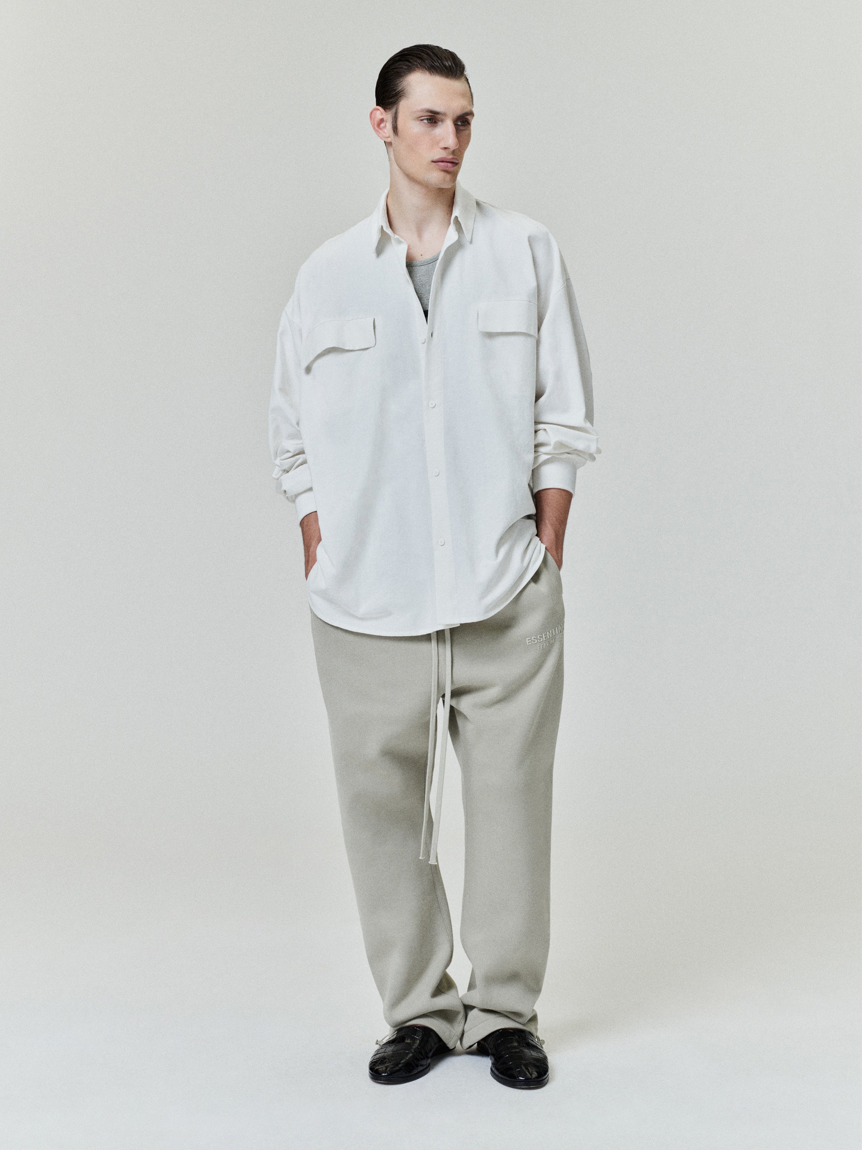 male model wearing oversized off-white cotton Oxford shirt with chest flap pockets and rolled-up sleeves standing front view