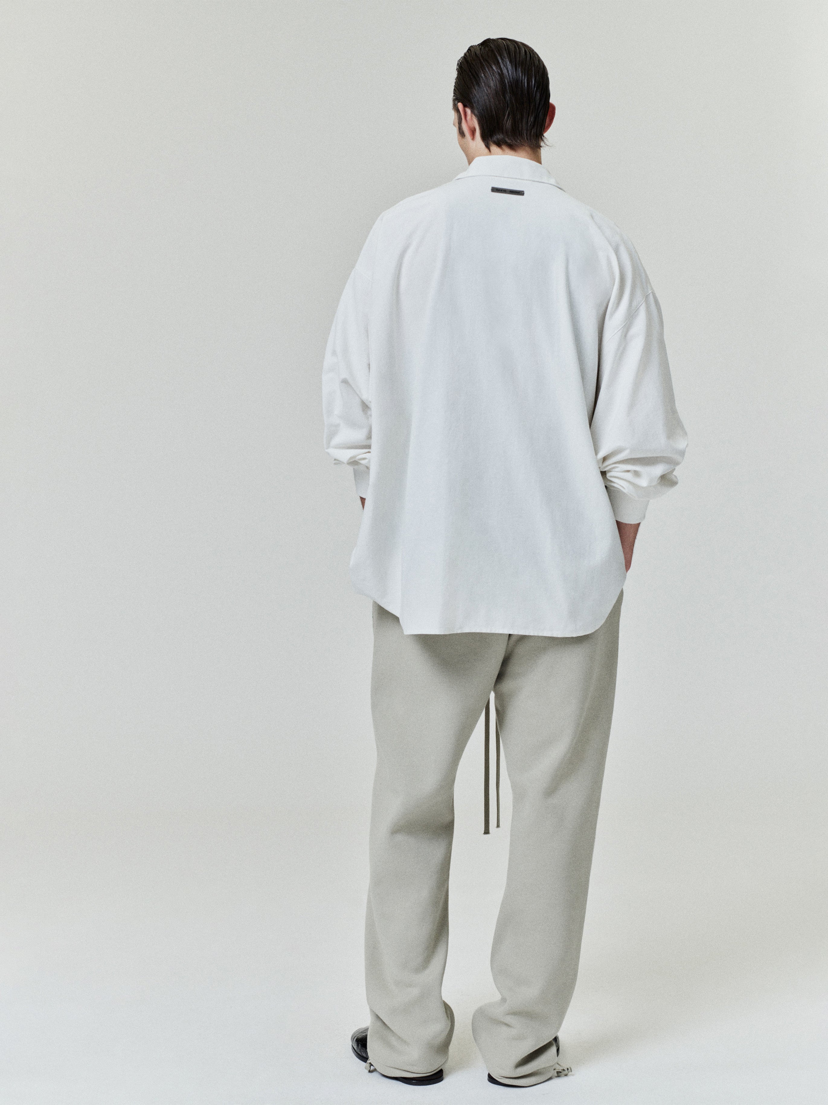 back view of male model wearing oversized off-white cotton Oxford shirt with long sleeves and relaxed fit
