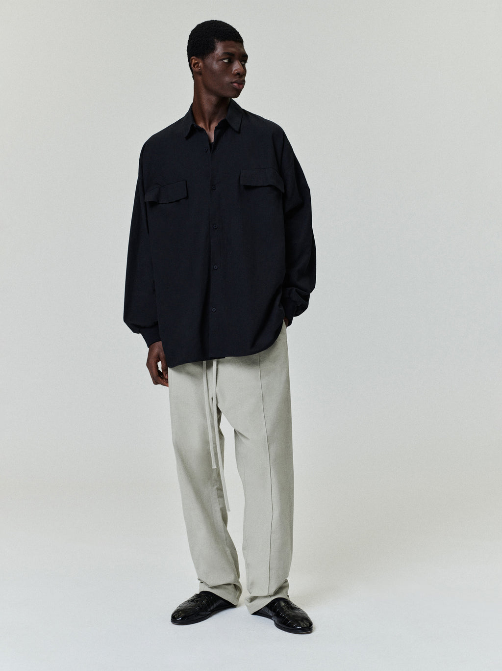 male model wearing oversized black cotton Oxford shirt with long sleeves and flap chest pockets in front view