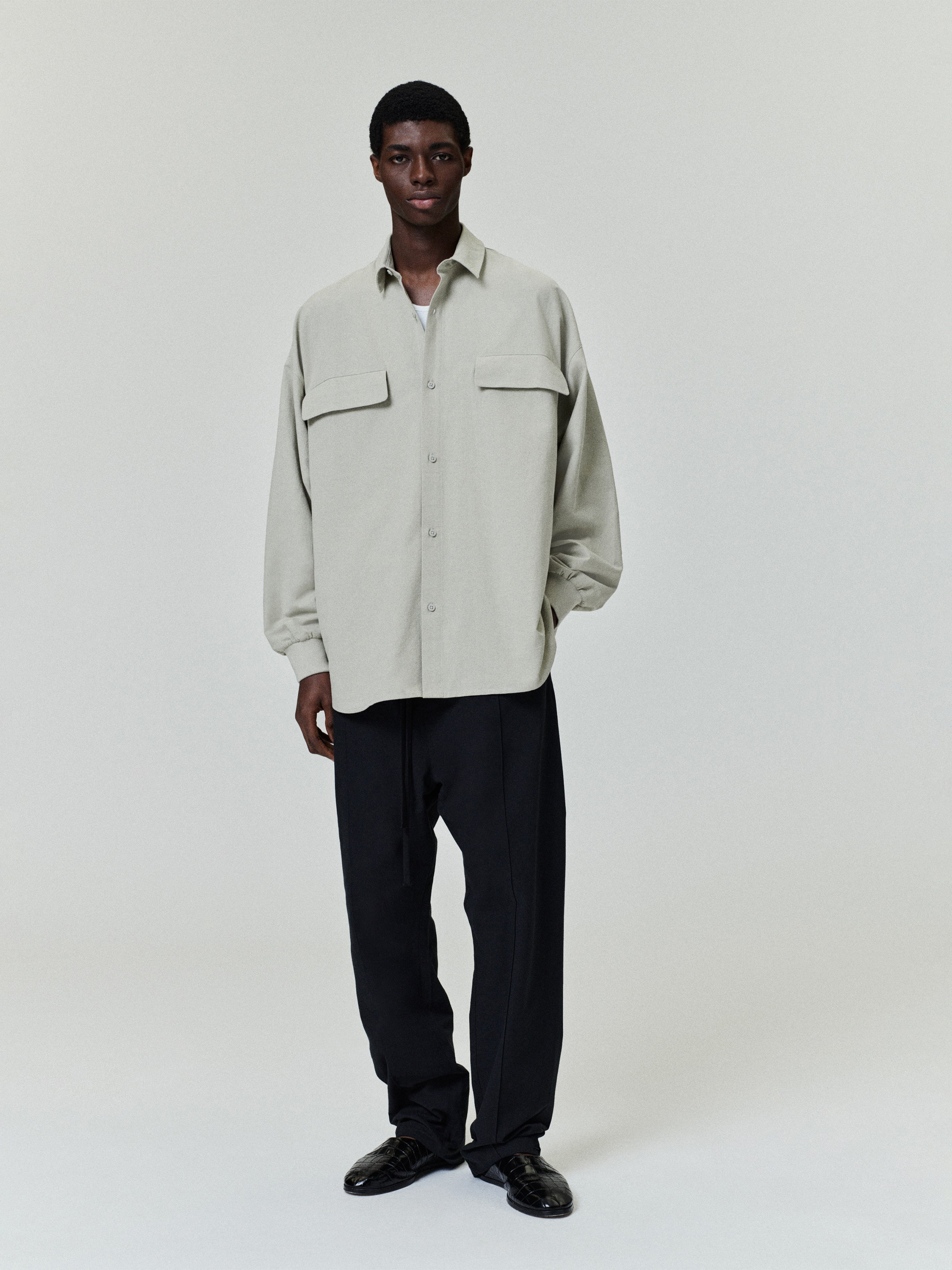 male model wearing oversized light grey Oxford shirt with flap chest pockets and long sleeves against plain background