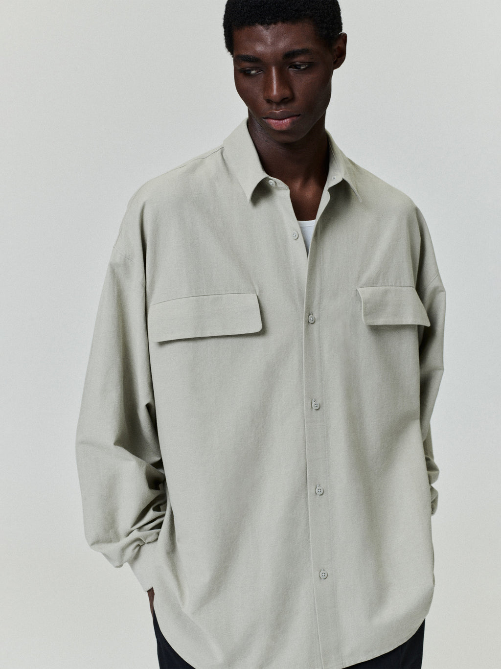 male model wearing oversized light beige Oxford shirt with long sleeves and flap pockets against plain background