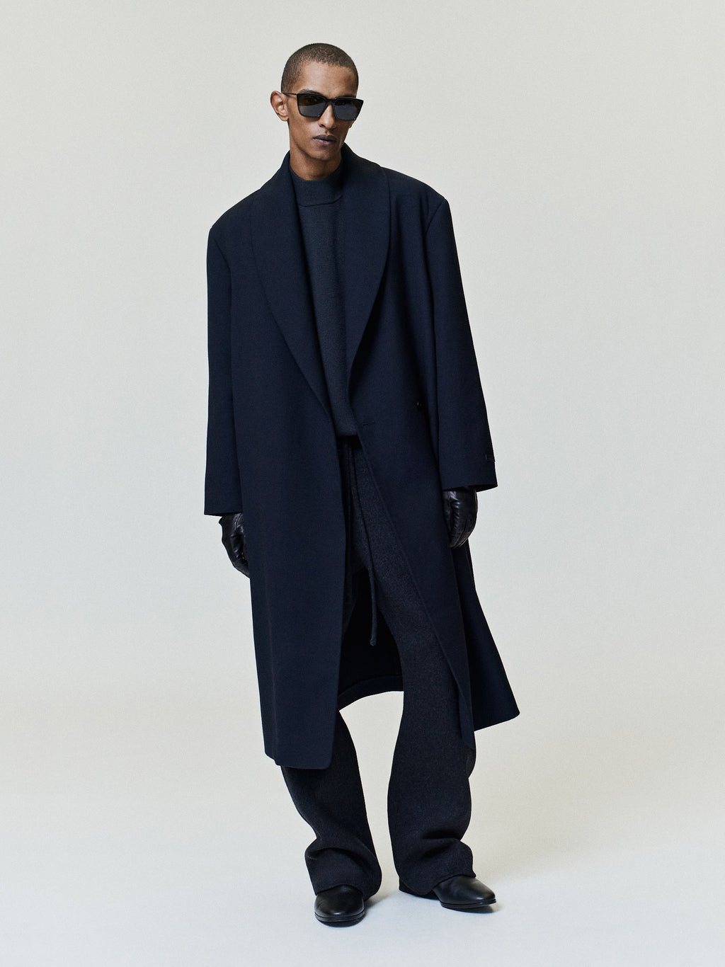 Merino Knit Mockneck Sweater modeled in black with a high neckline and long sleeves layered beneath a dark overcoat as Tops