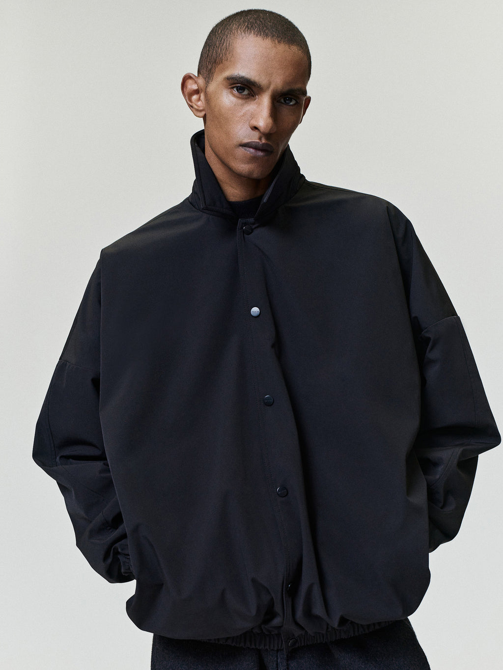 Bonded Nylon Tech Windbreaker in black worn by a model with a high collar snap button front gathered sleeves and elastic hem as Outerwear