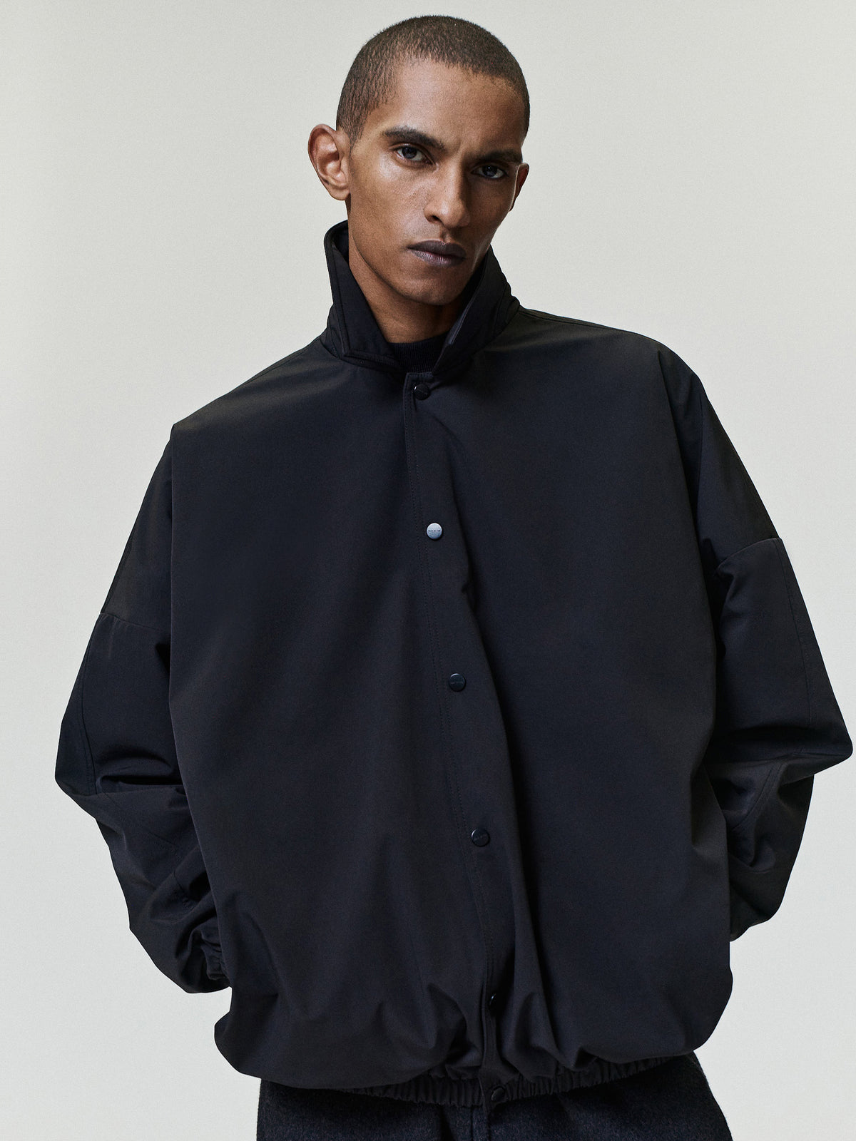 Bonded Nylon Tech Windbreaker in black worn by a model with a high collar snap button front gathered sleeves and elastic hem as Outerwear