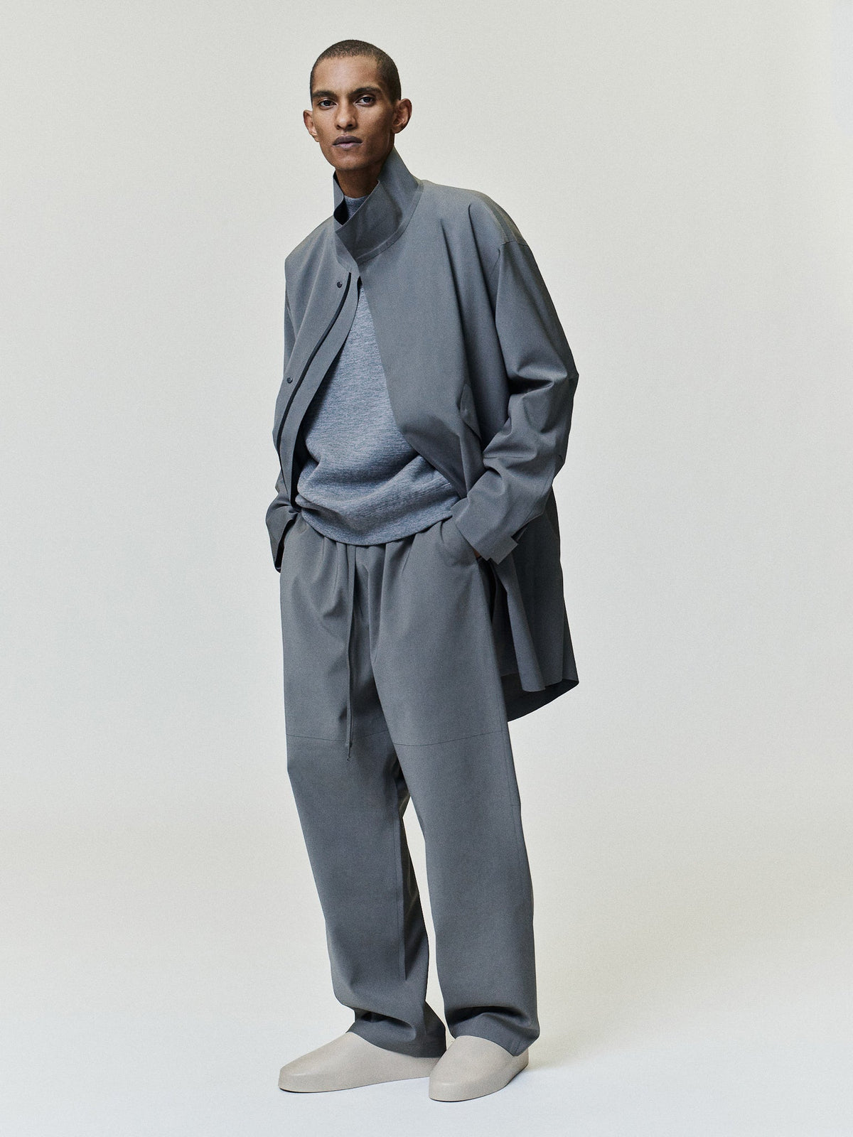 Merino Double Knit Mockneck Sweater in gray worn under a dark jacket with its mockneck collar and long sleeves visible as Tops
