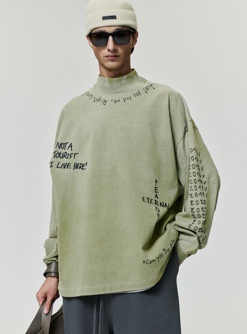 Hand Written Mockneck Long Sleeve Tee in sage green with handwritten black graphics worn by a model with dark trousers as Tops