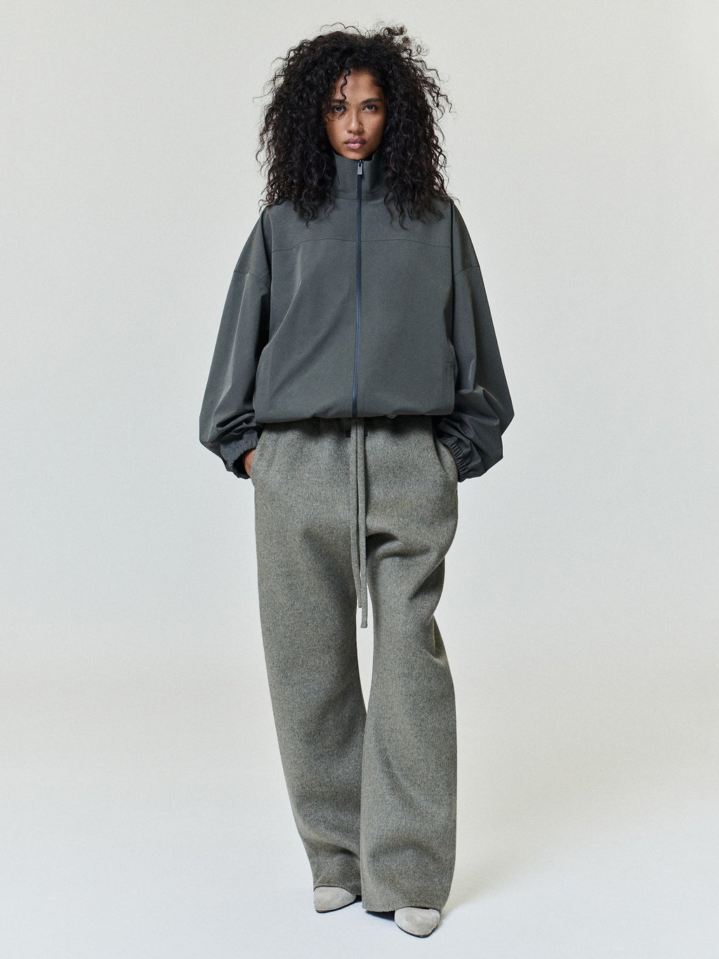 Bonded Nylon Track Jacket in charcoal worn by a model with a high zip collar elastic hem and long sleeves styled with gray wide leg trousers as Outerwear