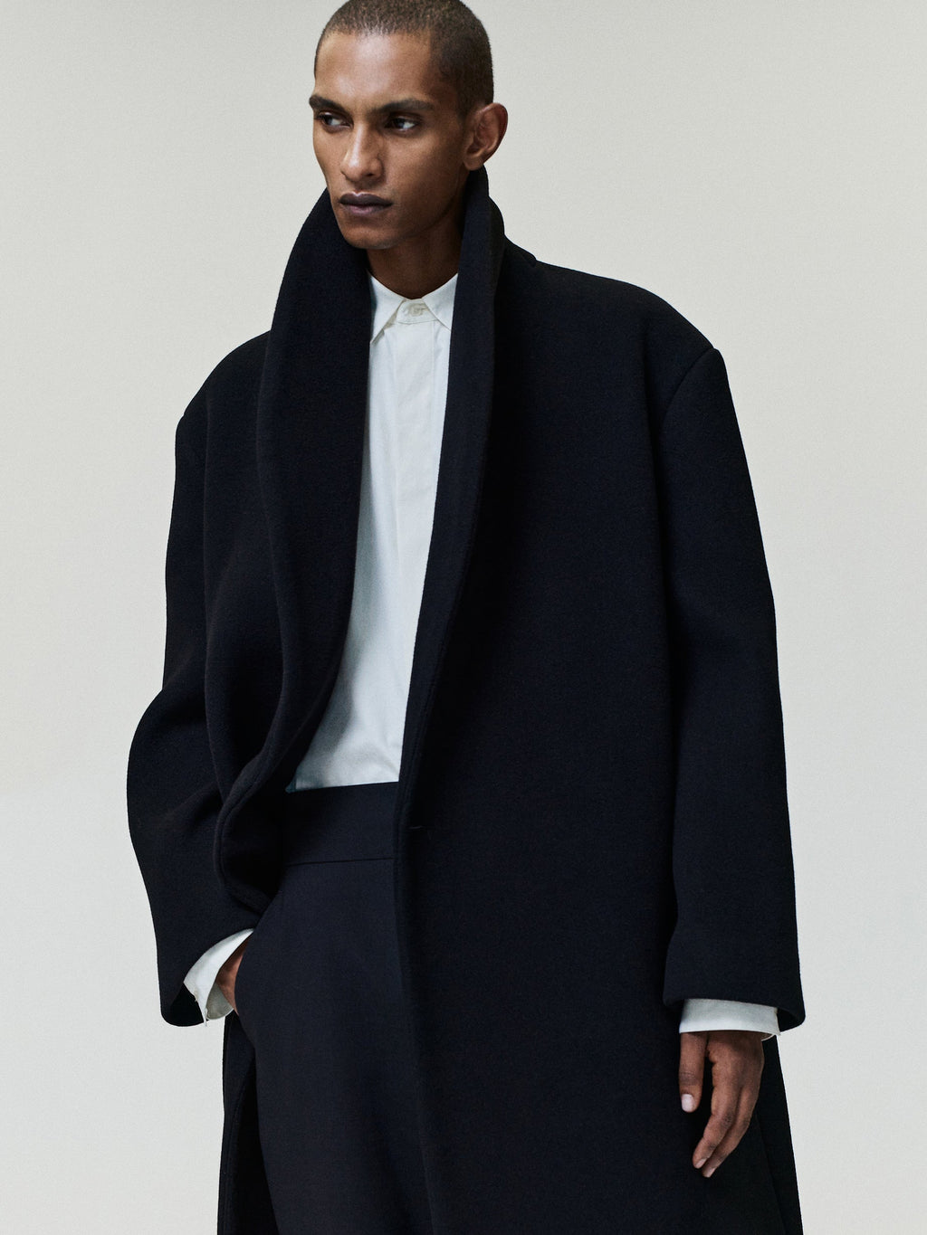 Melton Wool Shawl Overcoat in black worn by a model with a shawl collar open front long sleeves and relaxed longline fit as Outerwear