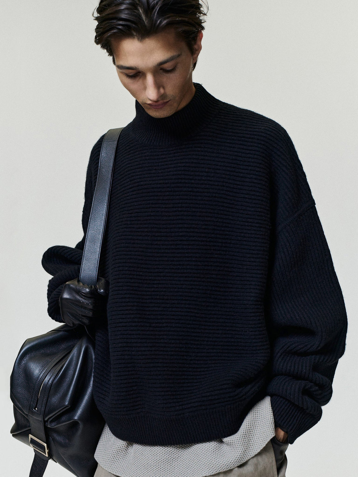 Wool Cashmere Rib Mockneck Sweater in black worn by a model with a ribbed collar and relaxed fit layered over a light gray top with a shoulder bag as Tops