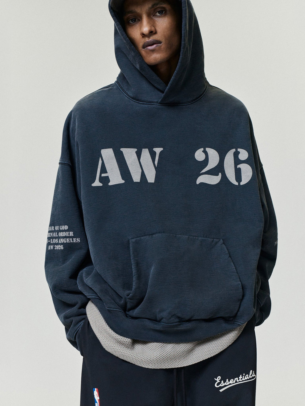 AW26 Vintage Pocket Hoodie in dark navy worn by a model with hood up oversized AW 26 chest lettering front pouch pocket and sleeve print as Tops