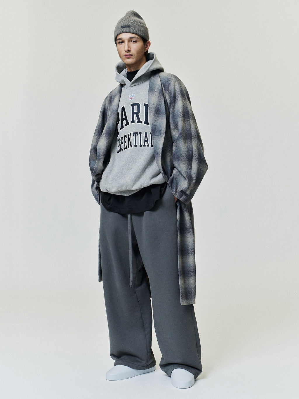 NFL Paris 90s Relaxed Hoodie in gray with Paris Essential chest lettering styled under a plaid overshirt with wide leg trousers and white shoes Tops