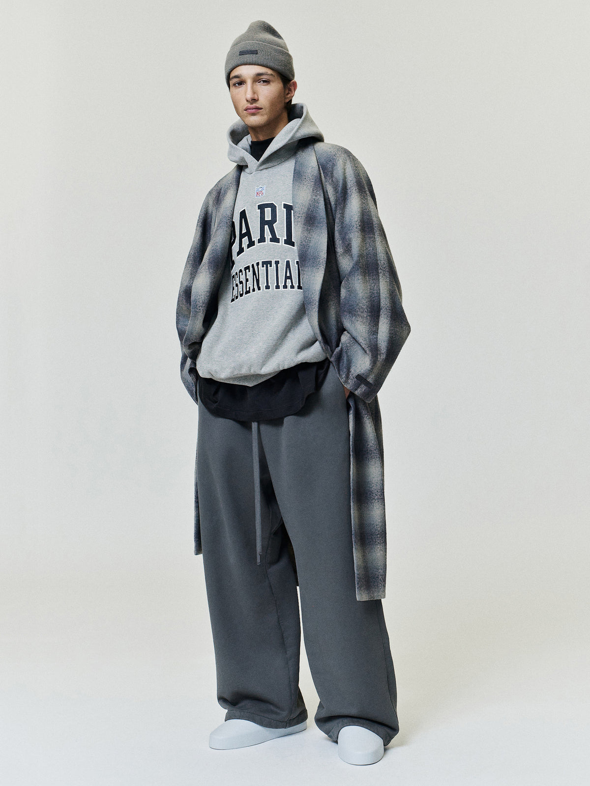 NFL Paris 90s Relaxed Hoodie in gray with Paris Essential chest lettering styled under a plaid overshirt with wide leg trousers and white shoes Tops