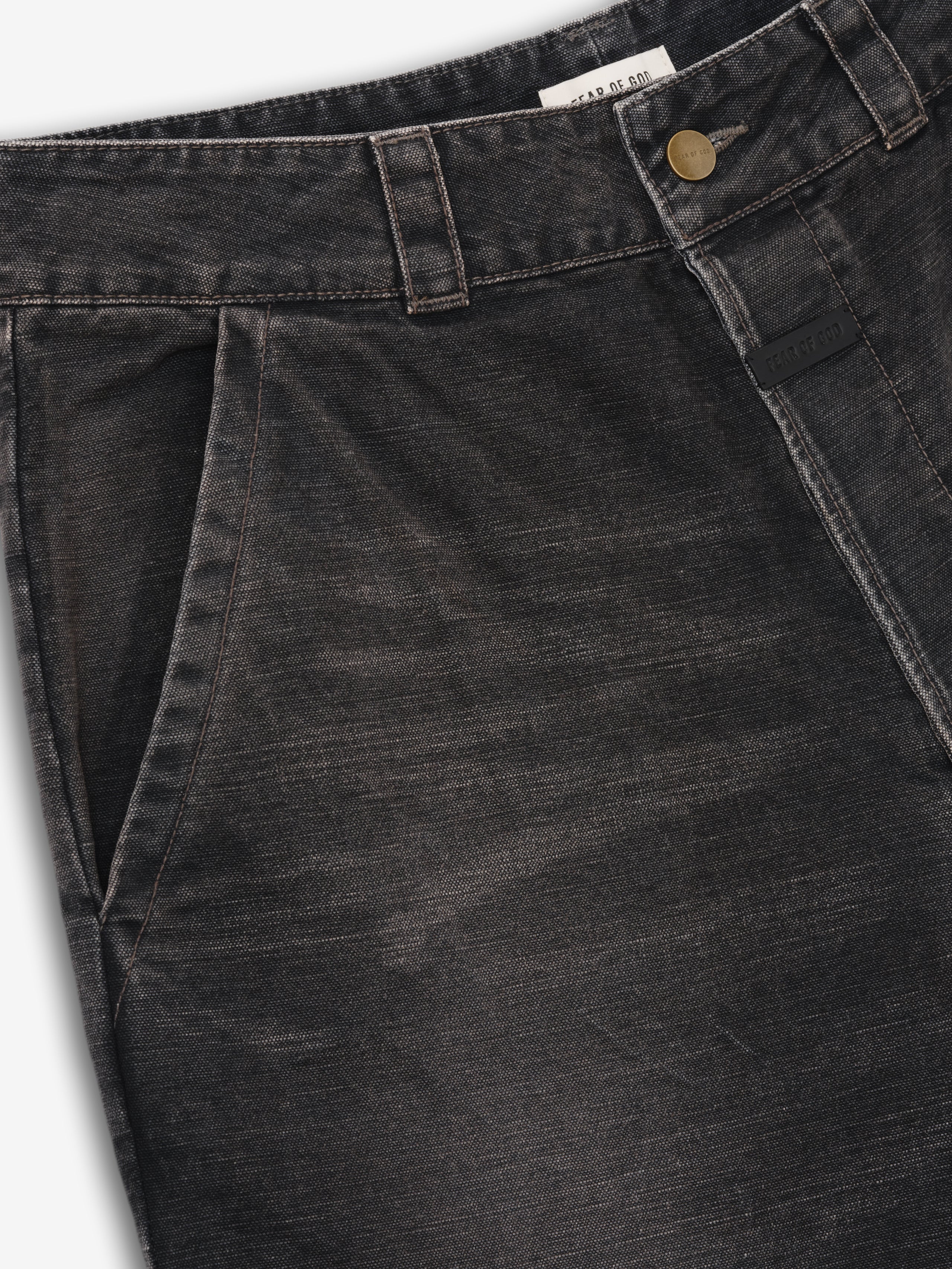 close-up of black washed cotton canvas utility pants waistband with side pocket and antique brass button closure