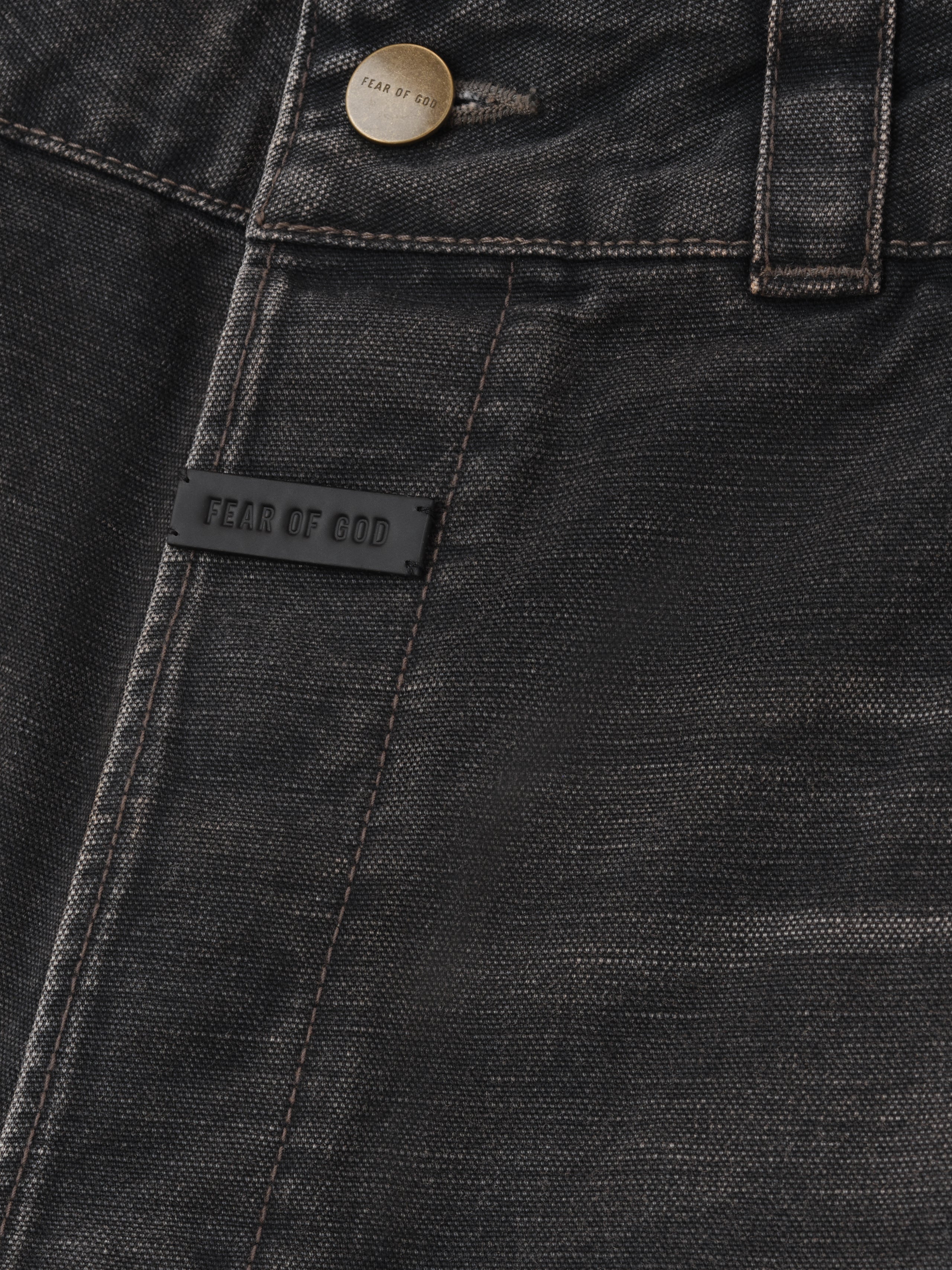 close-up of black cotton canvas utility pants front pocket with branded rubber tag and antique metal button closure
