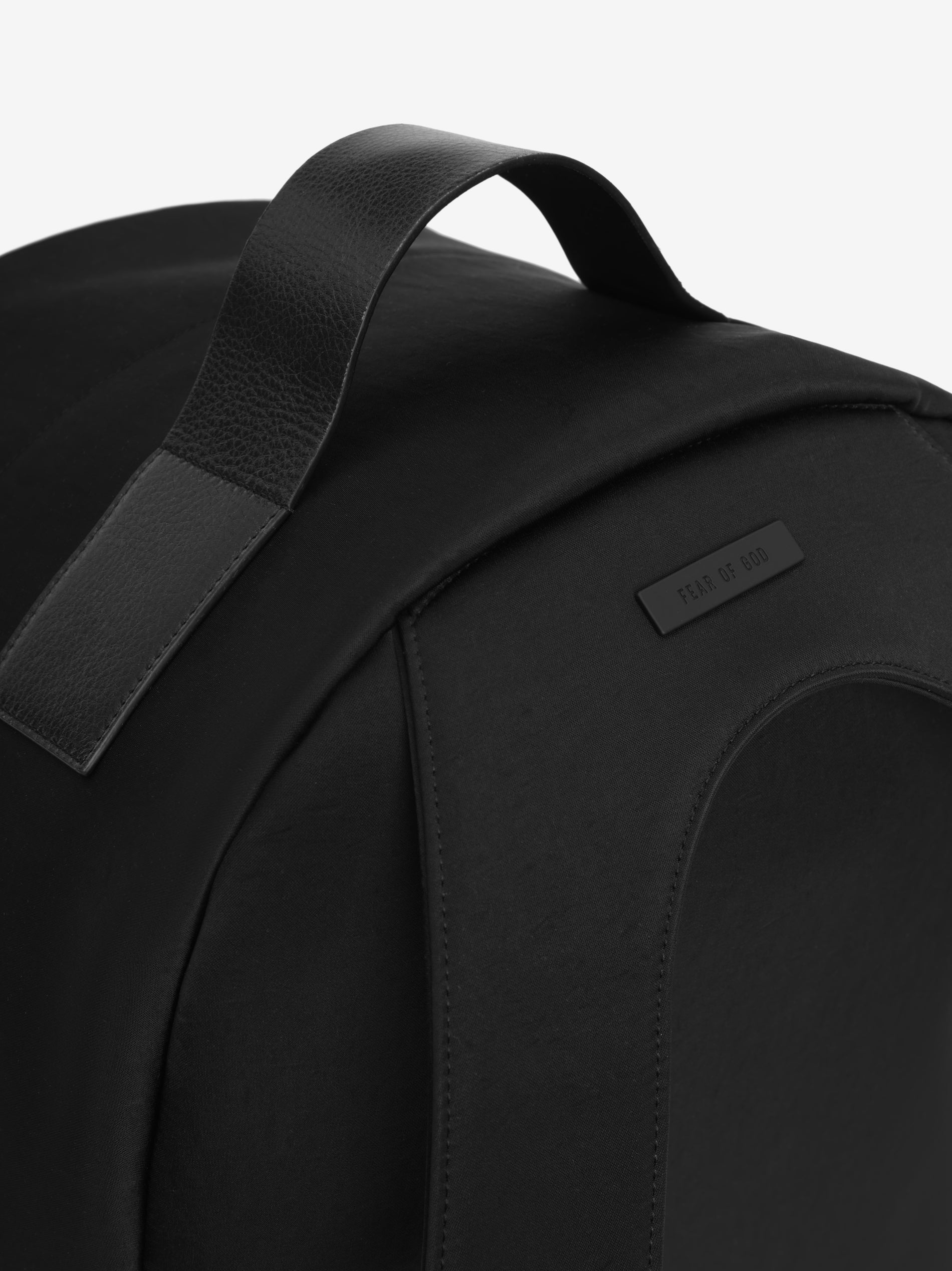 close-up of black technical nylon backpack leather top handle and subtle Fear of God logo patch on curved panel