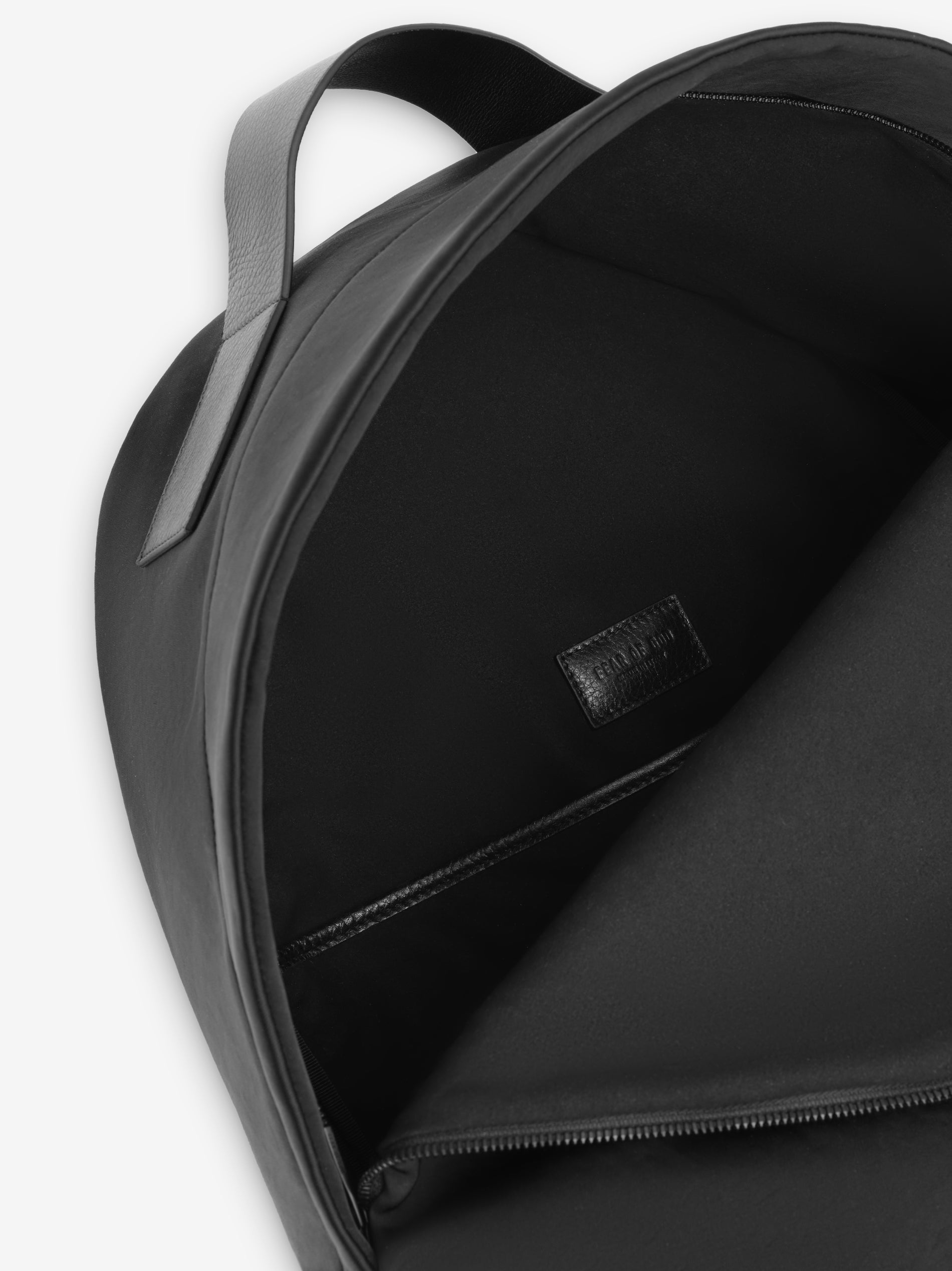interior view of black nylon backpack showing smooth lining zip pocket and leather top handle close-up