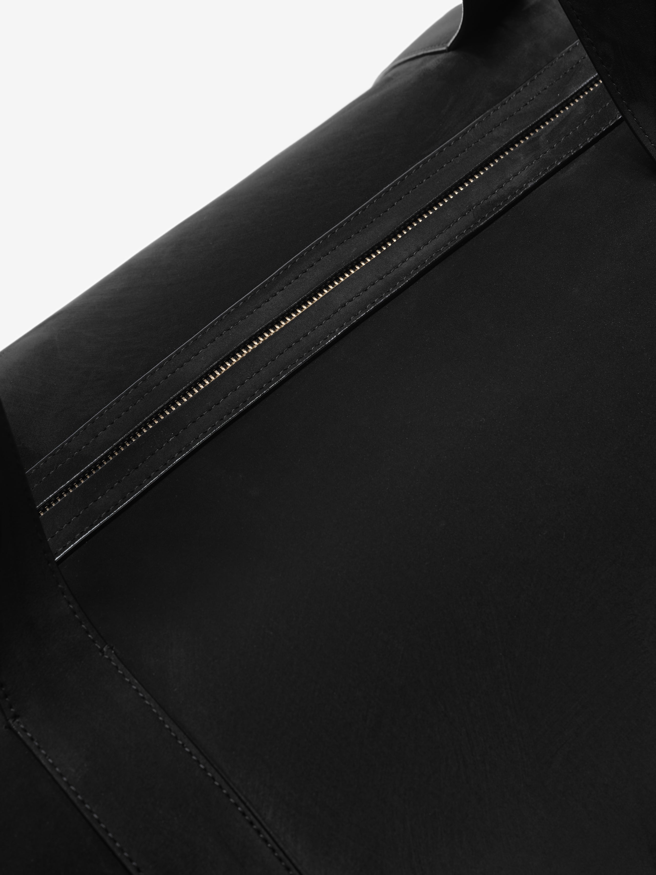 Close-up of the Large Belted Duffle in black, highlighting a sleek leather zipper detail with fine stitching and a smooth matte finish on the cylindrical body.