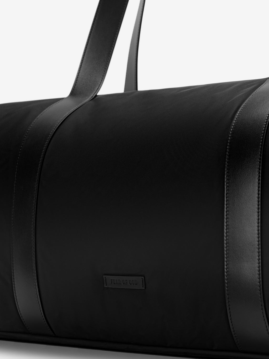Close-up of a smooth black nylon duffle bag with wide leather straps and a small rectangular logo patch