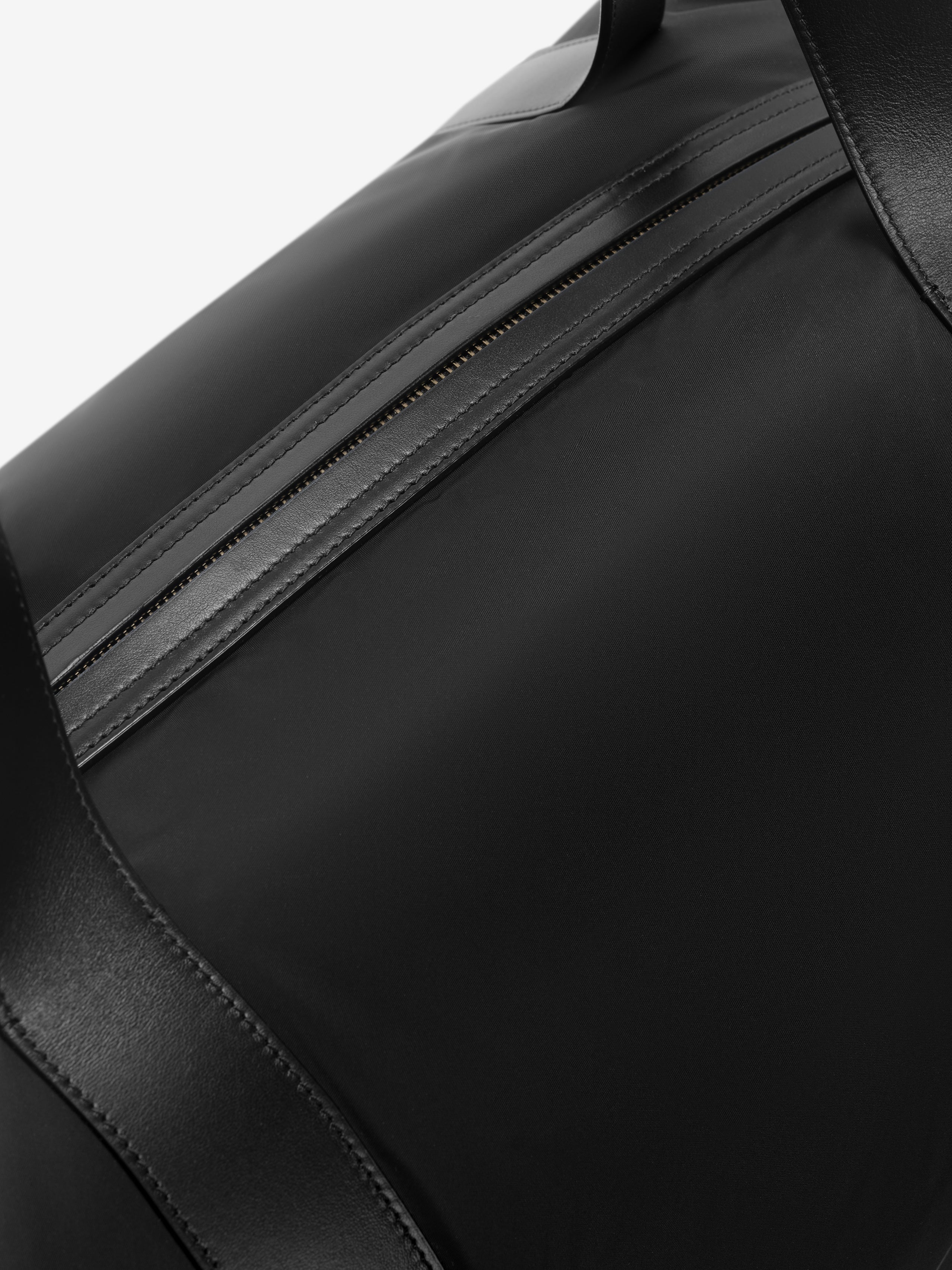 Close-up of black nylon duffle bag featuring a sleek leather-trimmed zipper and wide leather handles