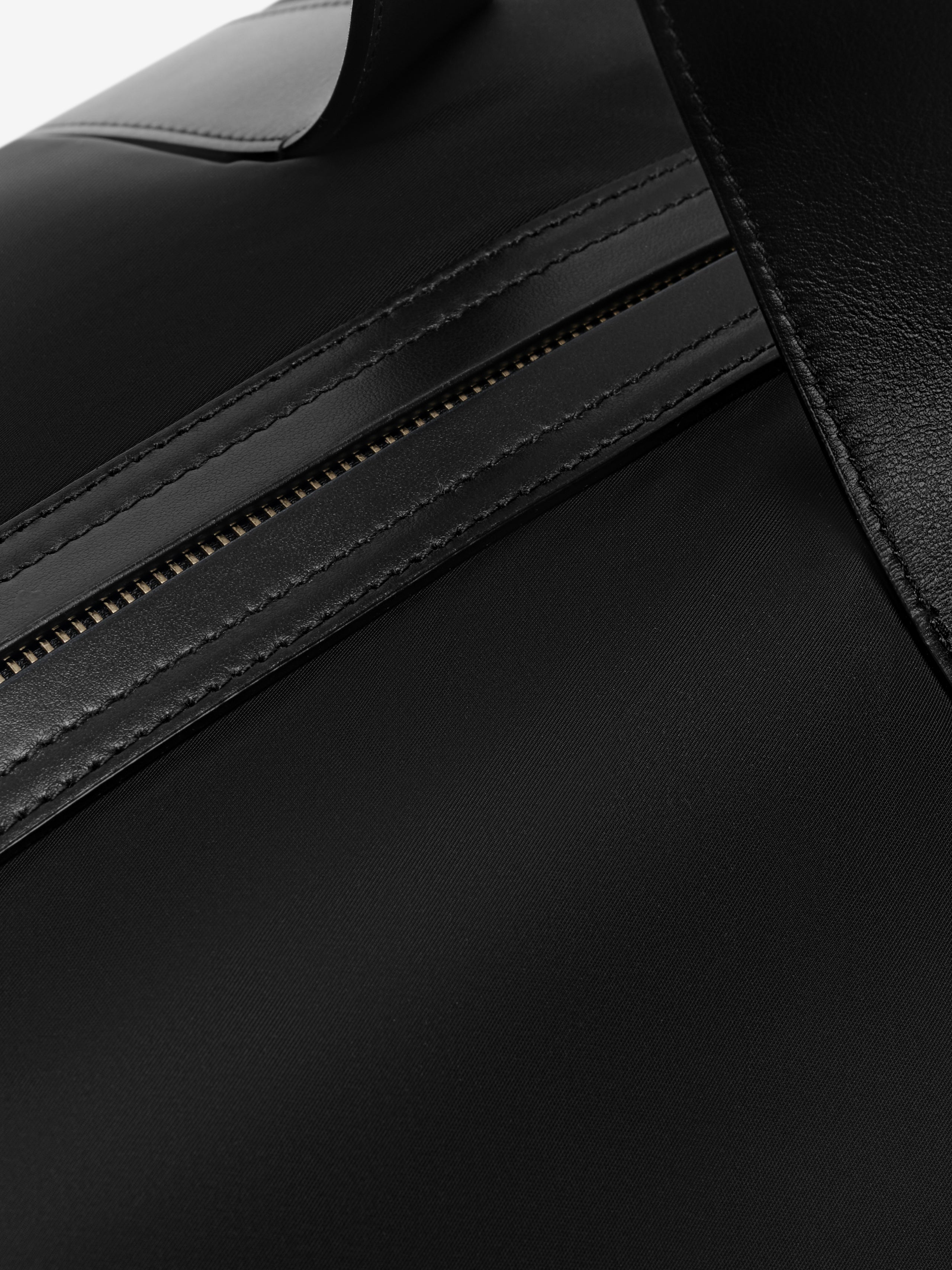 Close-up of black bag zipper with smooth leather trim and detailed stitching on durable nylon fabric surface